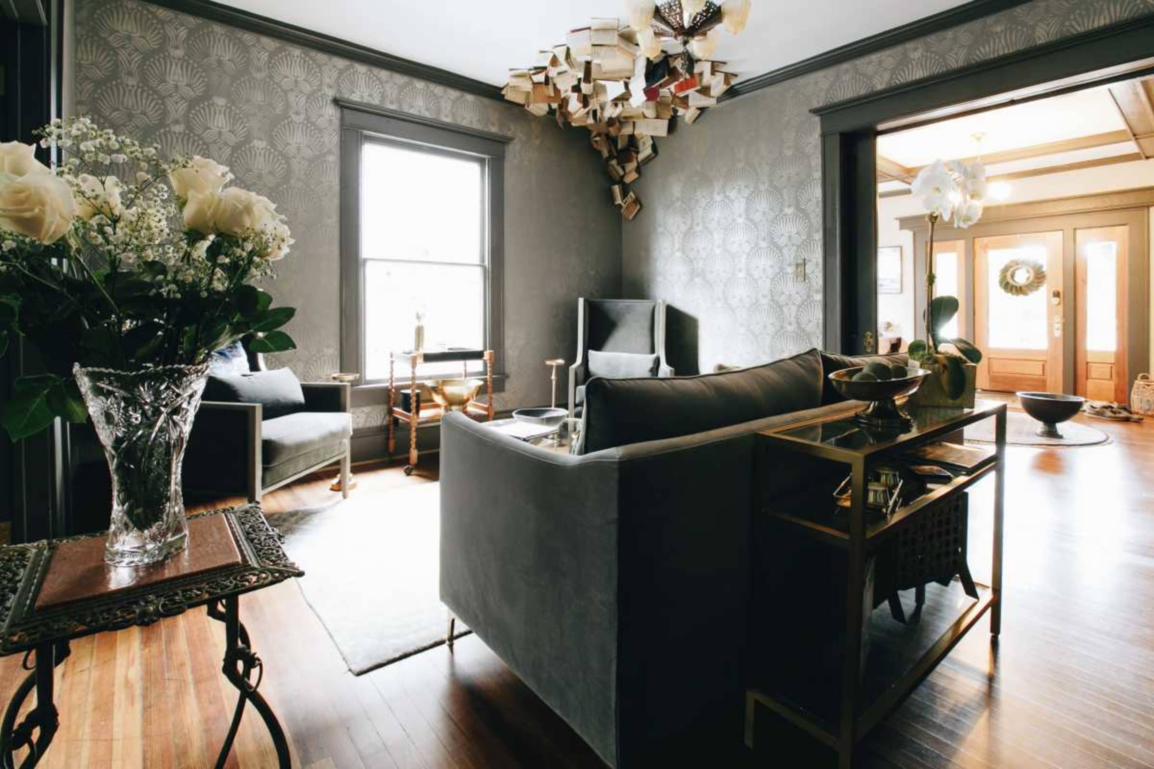 The image shows a stylish living room with gray walls, a contemporary chandelier made of books, and elegant furniture including a sofa and armchairs.