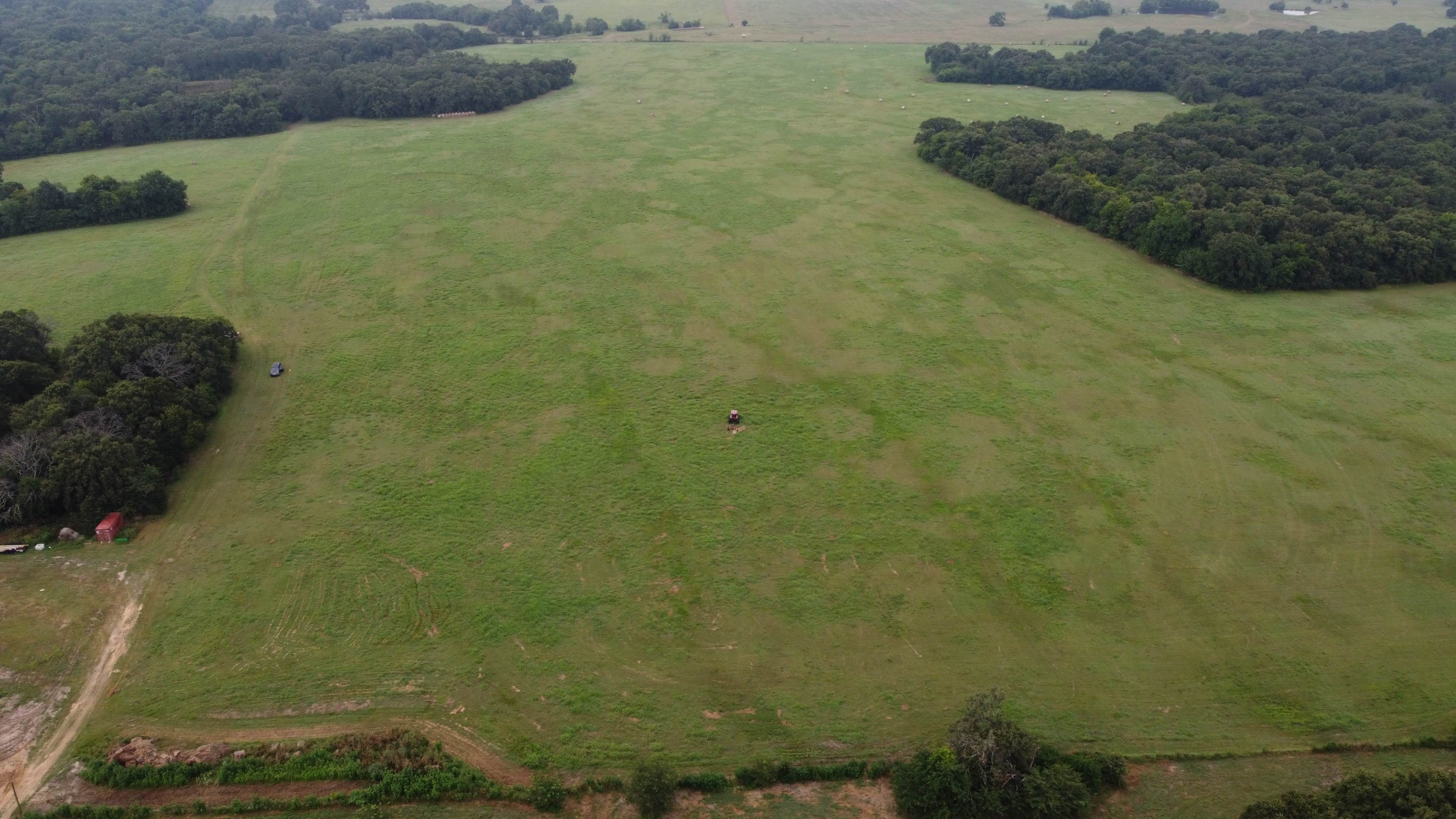 An aerial view of a large, open green field bordered by patches of trees.