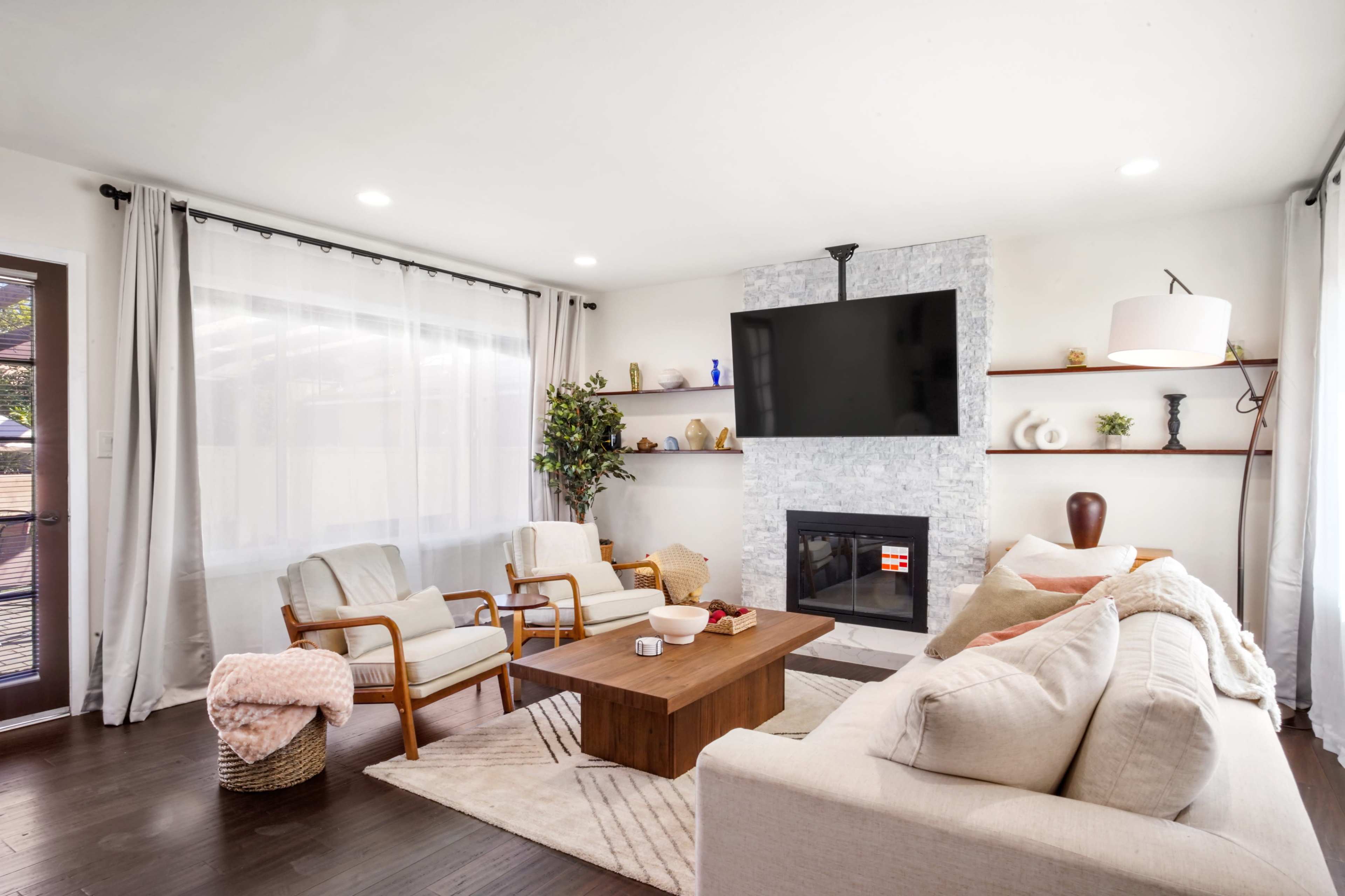 A modern living room with a stone fireplace, a wall-mounted TV, a coffee table, and seating arrangements with two chairs and a sofa.