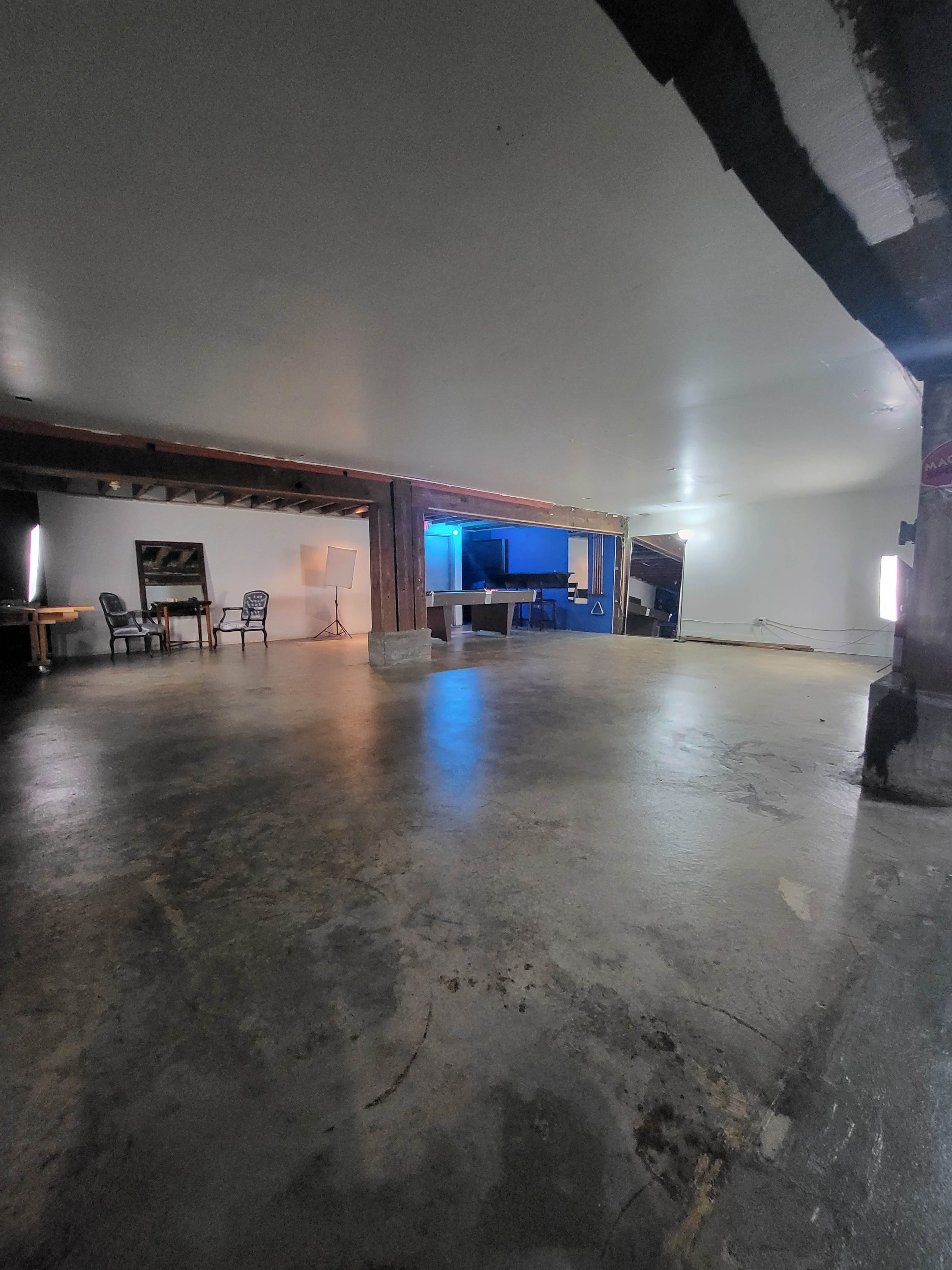 A spacious, empty room with a concrete floor, exposed beams, and minimal lighting.