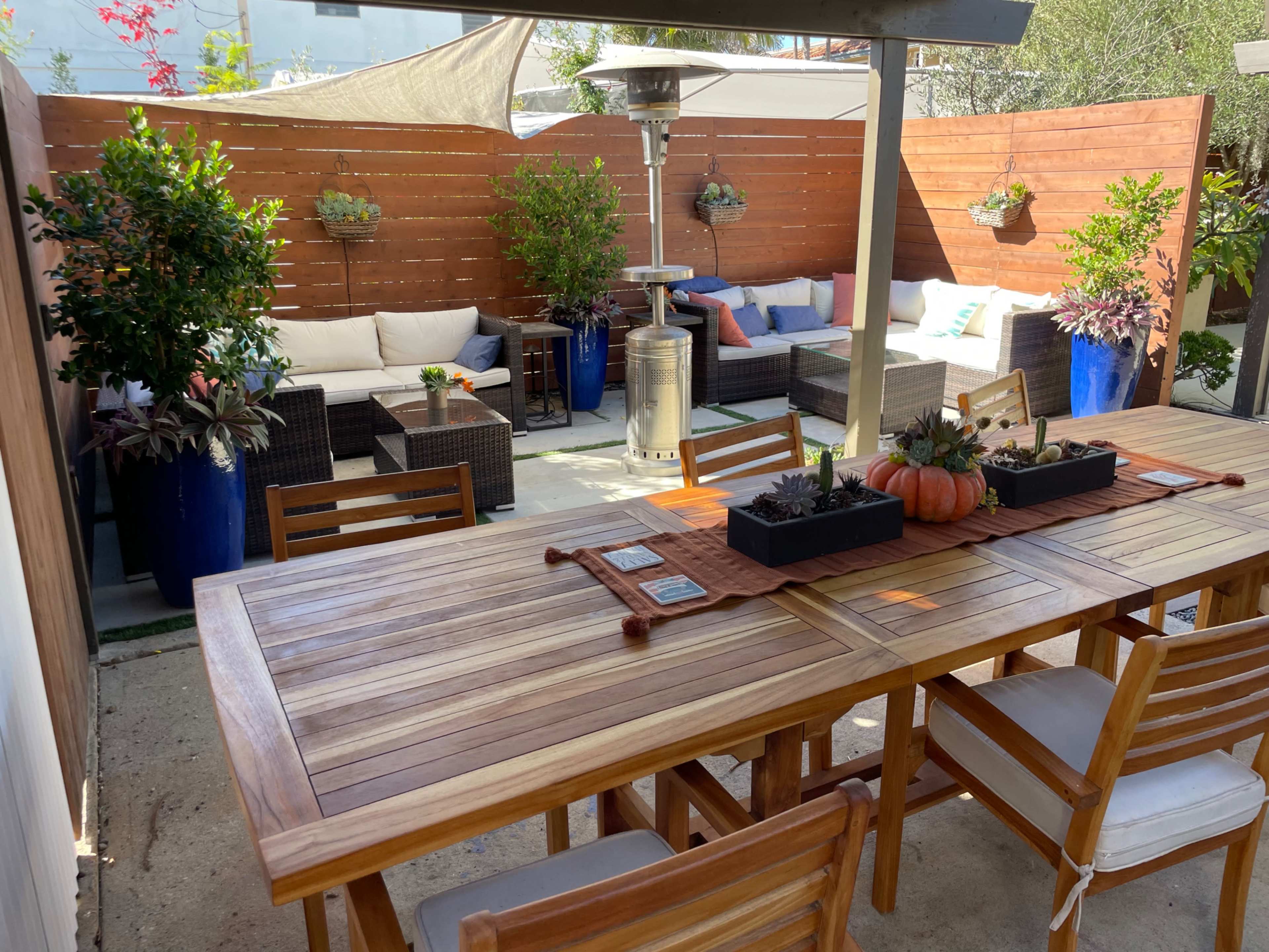 A spacious outdoor patio area featuring a wooden dining table, comfortable seating arrangements, and potted plants.