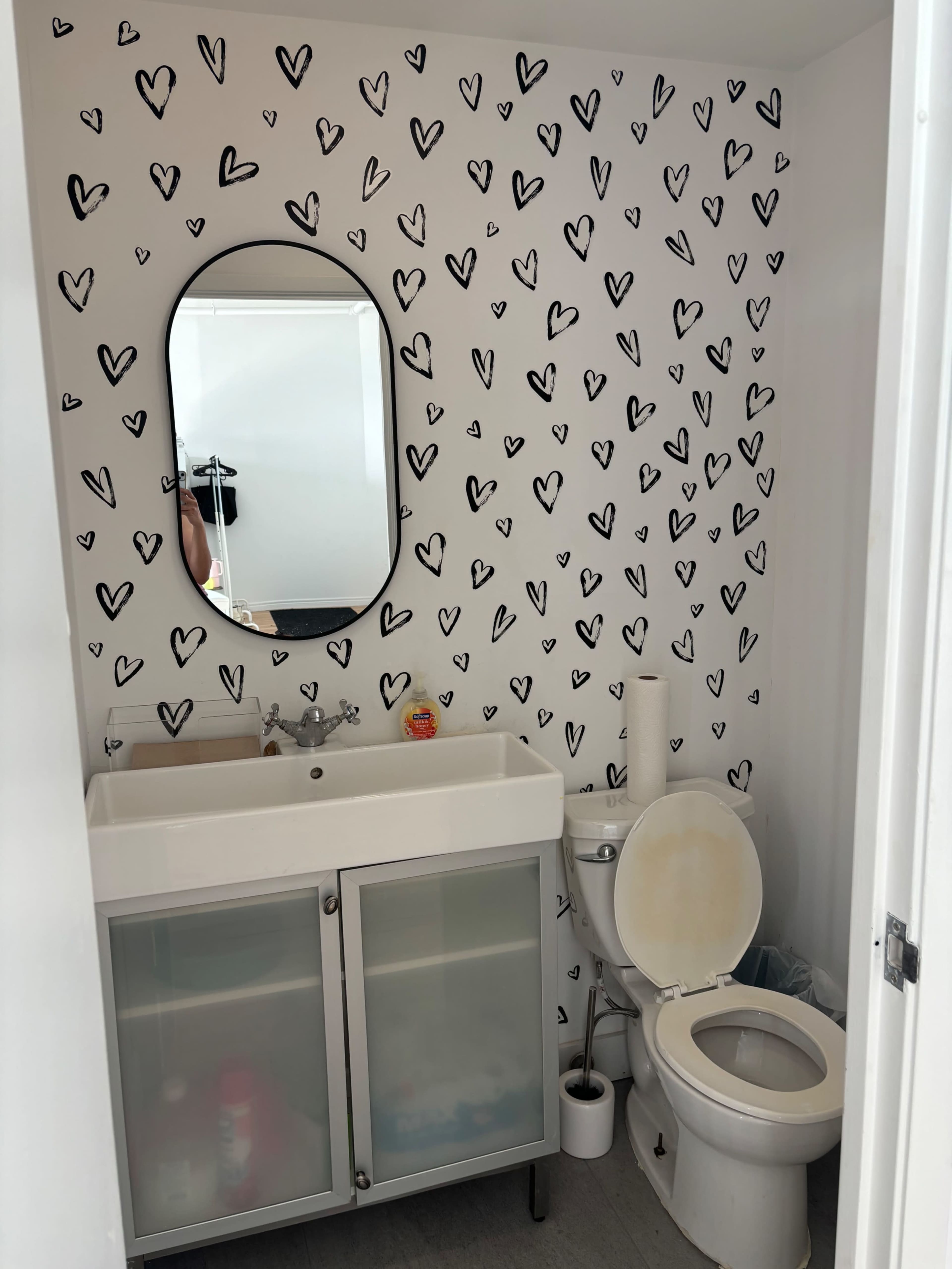 A small bathroom featuring a sink with a mirrored cabinet above it, a toilet, and walls decorated with black heart shapes.