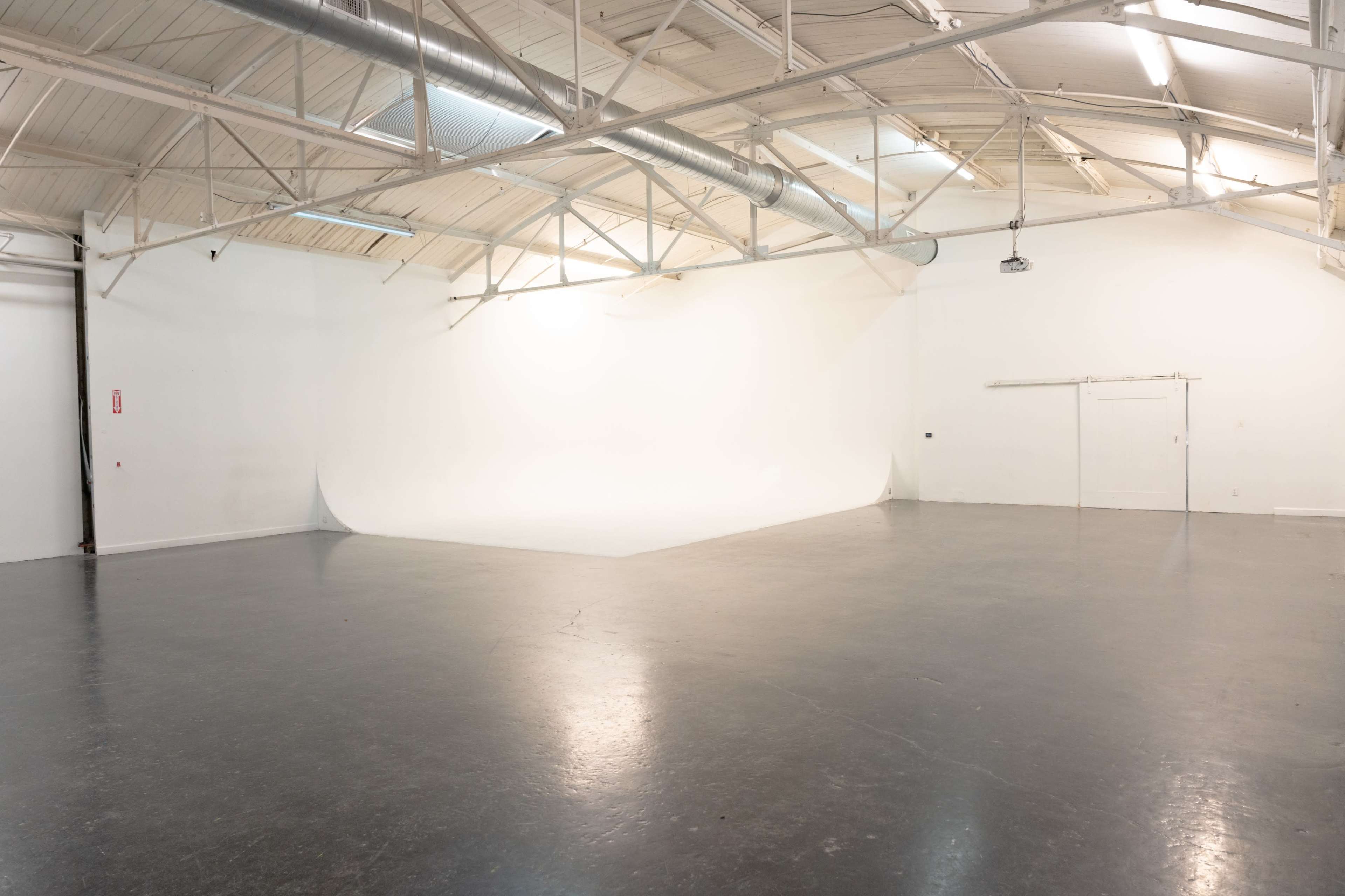 The image shows a spacious, empty studio with a smooth, white backdrop and polished concrete flooring.