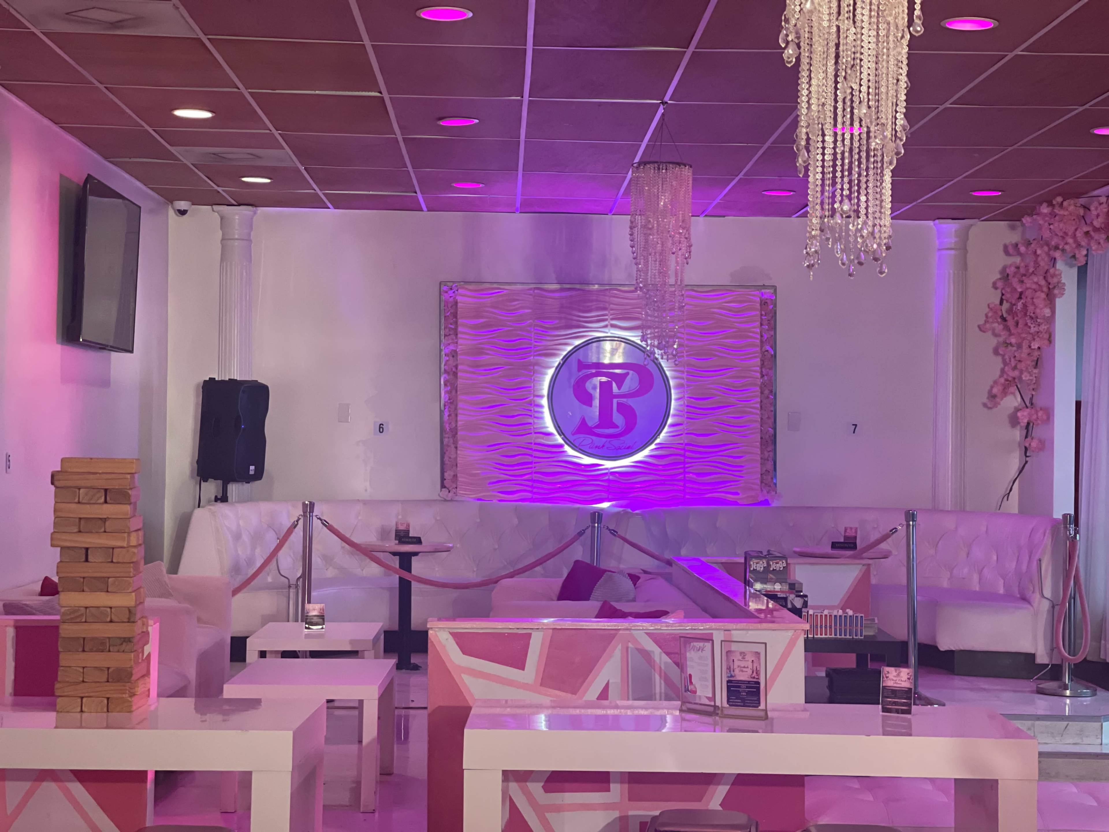 The interior of a stylish lounge featuring pink and white decor, plush seating, and a prominent logo on a textured wall.