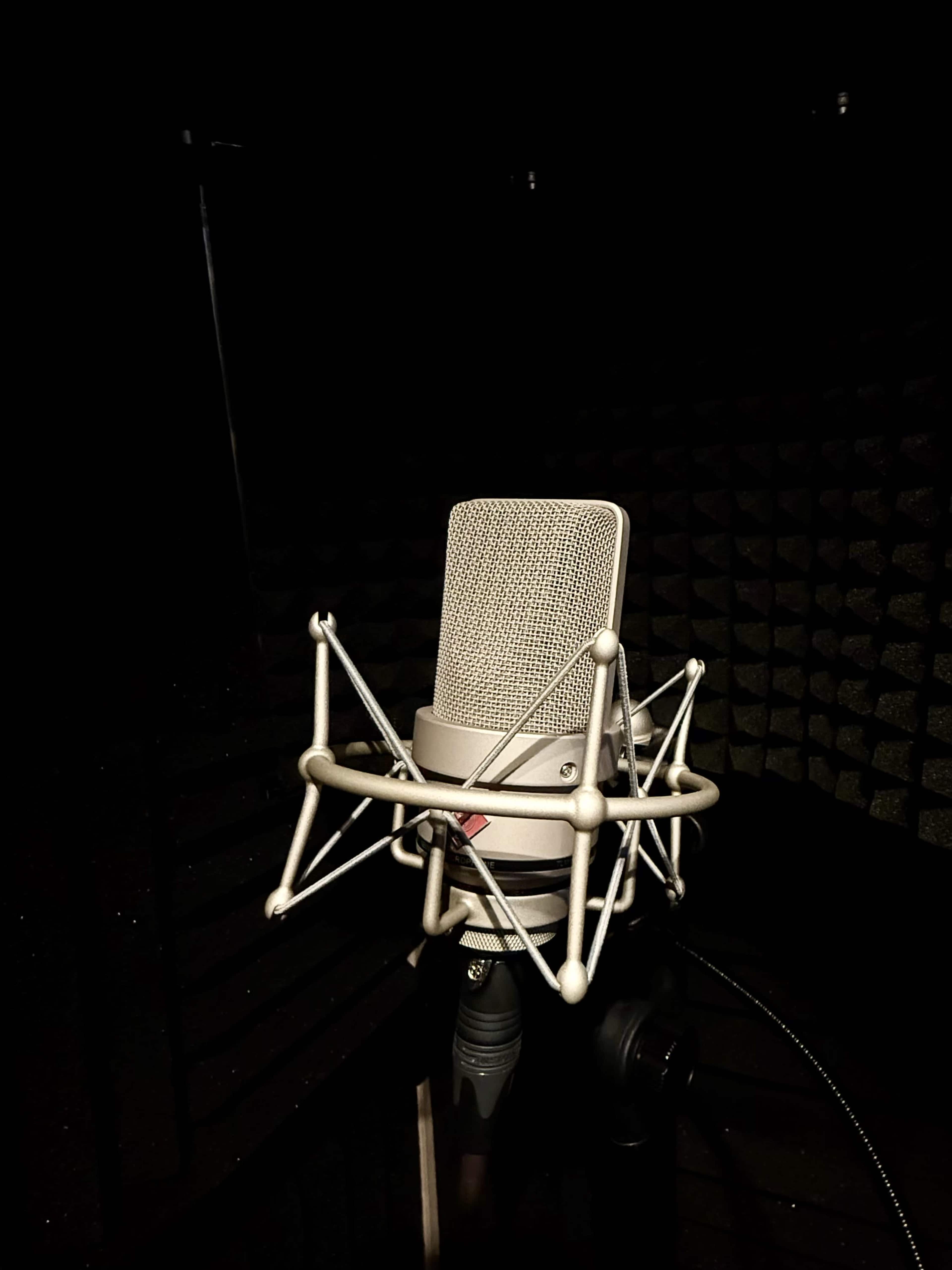 A microphone stands in a dark recording studio surrounded by soundproofing panels.