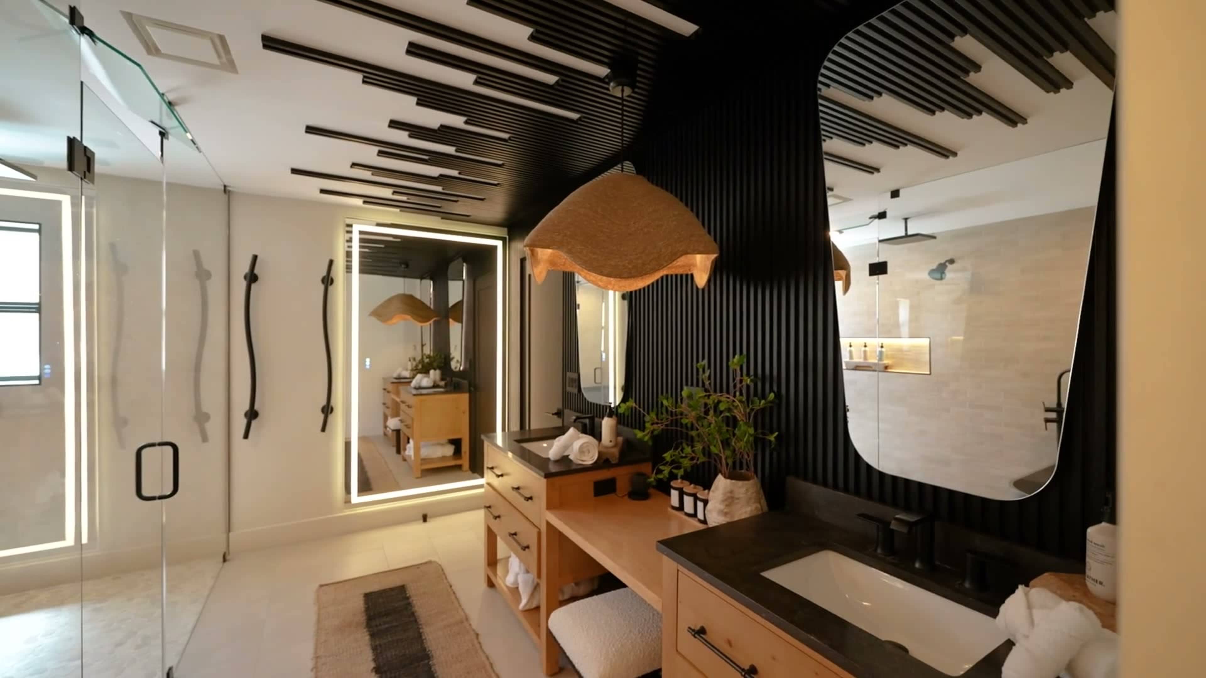 The image shows a modern bathroom with a sleek design featuring a wooden vanity, a large mirror, and unique ceiling details.
