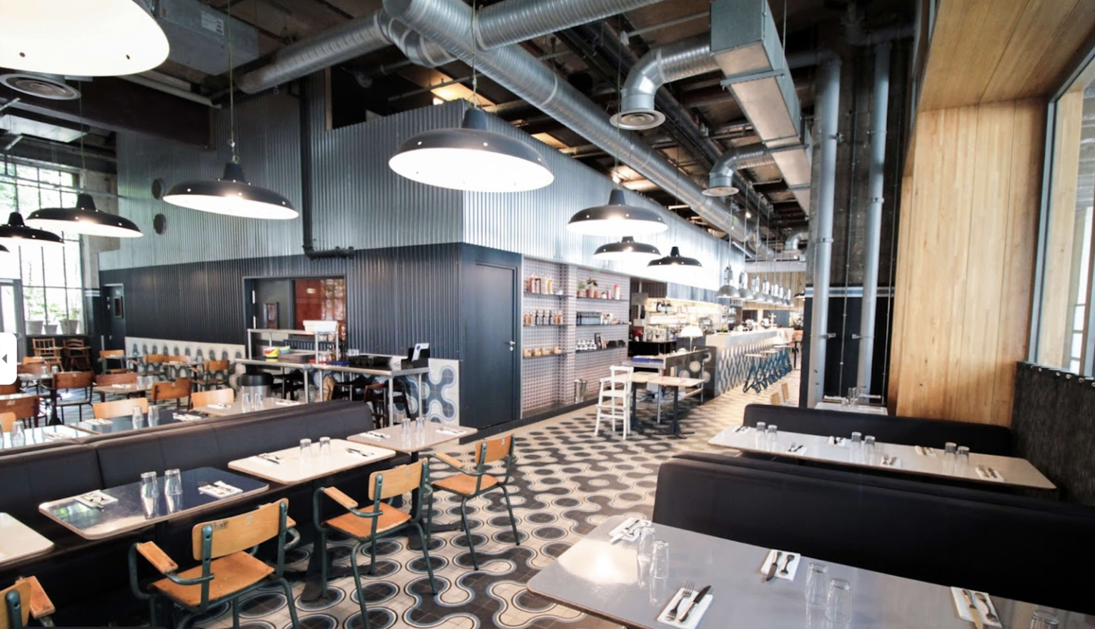 A spacious restaurant interior with a modern design, featuring rows of tables and booths, industrial-style lighting, and a long service counter.
