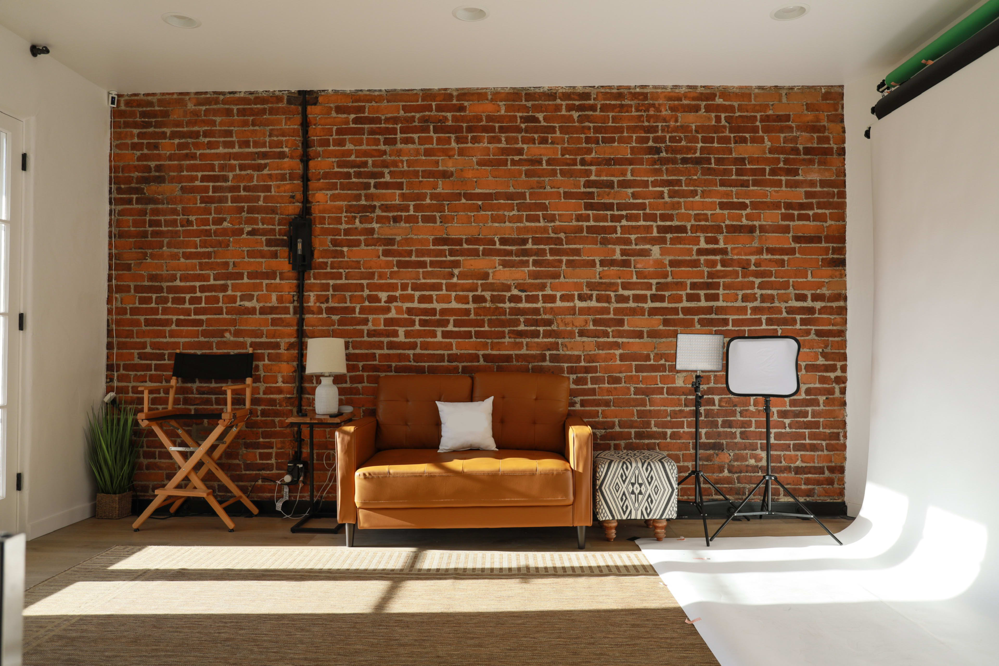 A cozy studio space featuring a brown couch, plants, and studio lights against a brick wall.