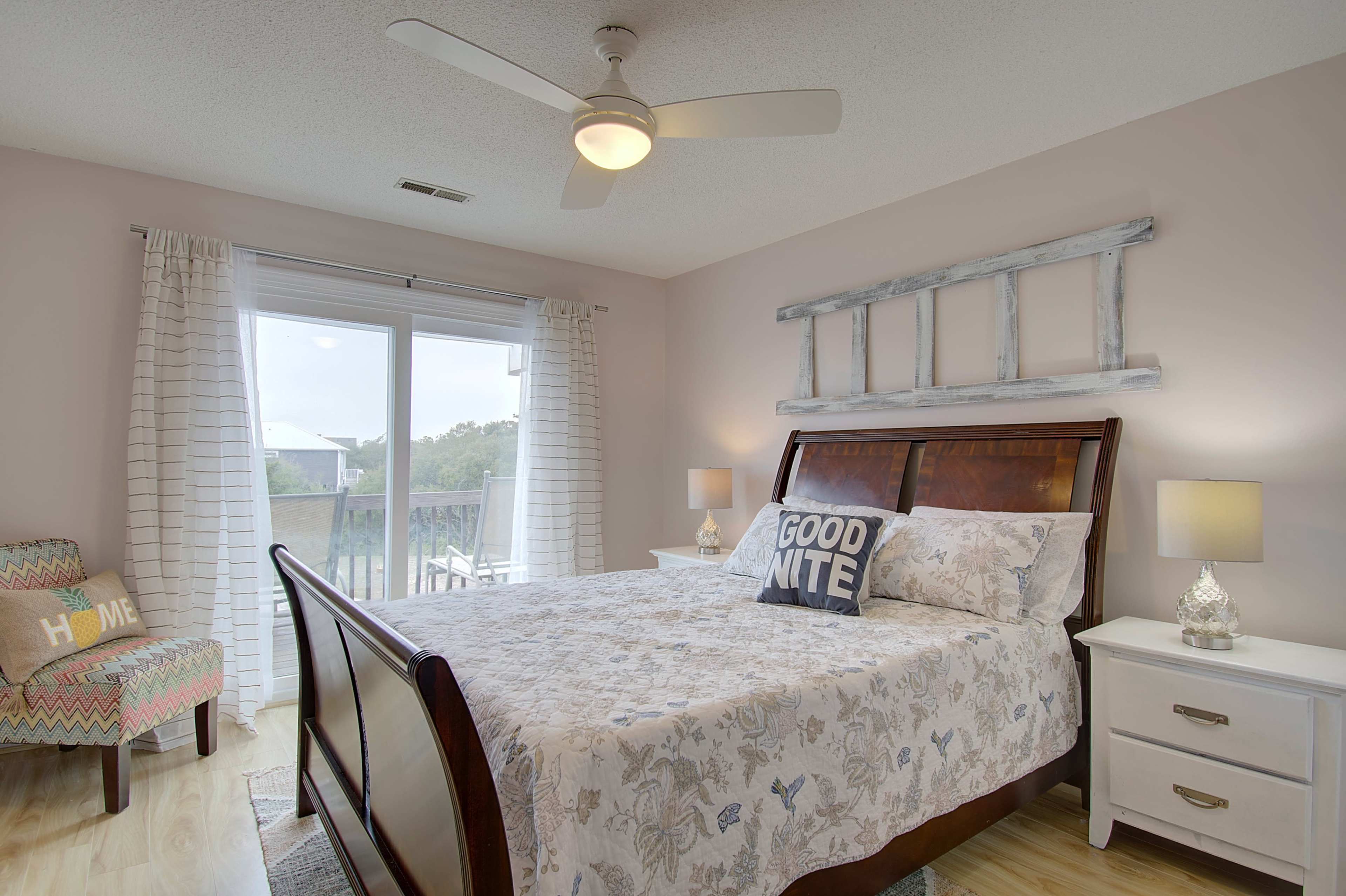 The bedroom features a large bed with a quilted cover, a decorative pillow that says "GOOD NITE," and is illuminated by two bedside lamps, with a view of a balcony through sliding glass doors.