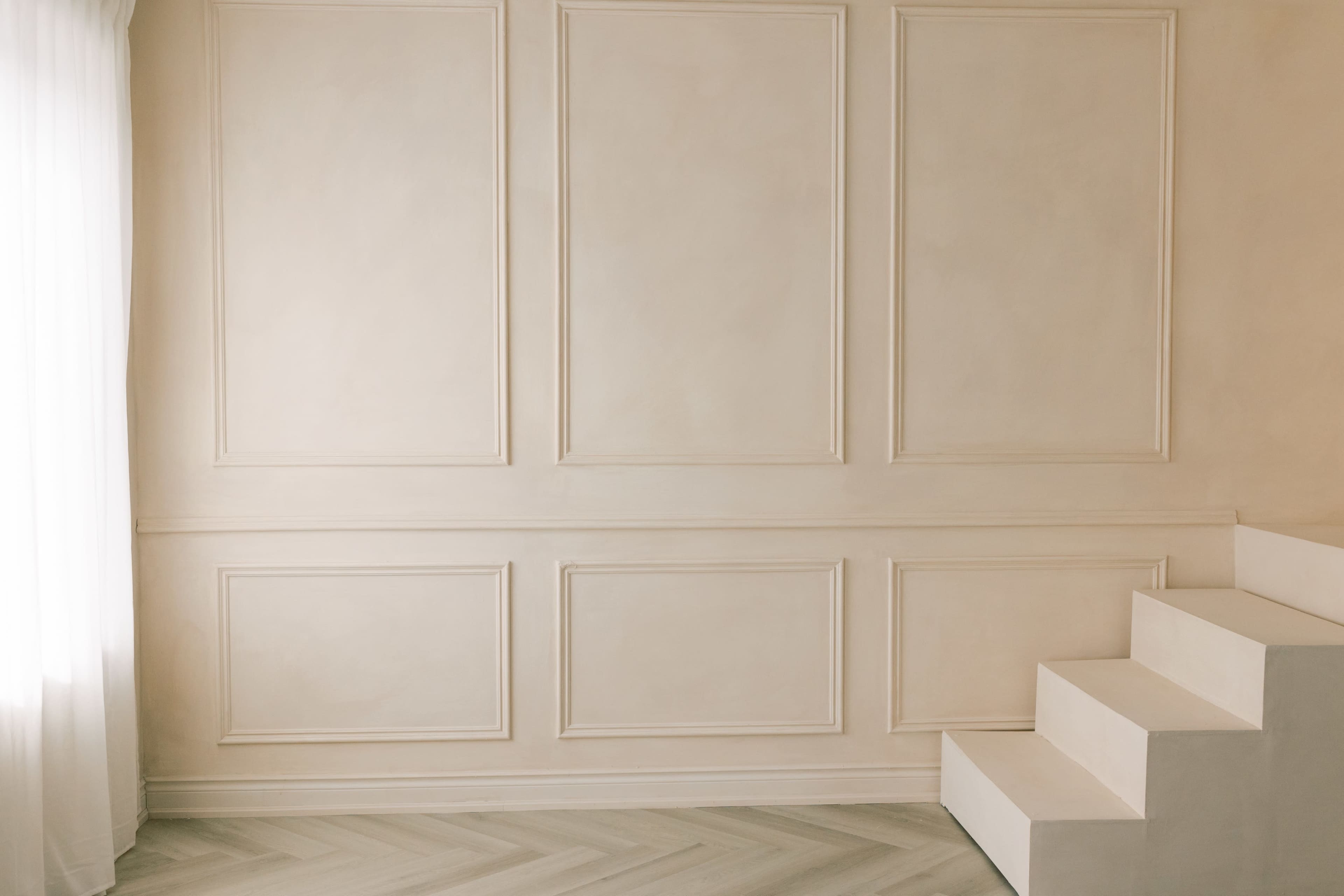 A light-colored room features panelled walls and a set of white stairs leading to an upper level.