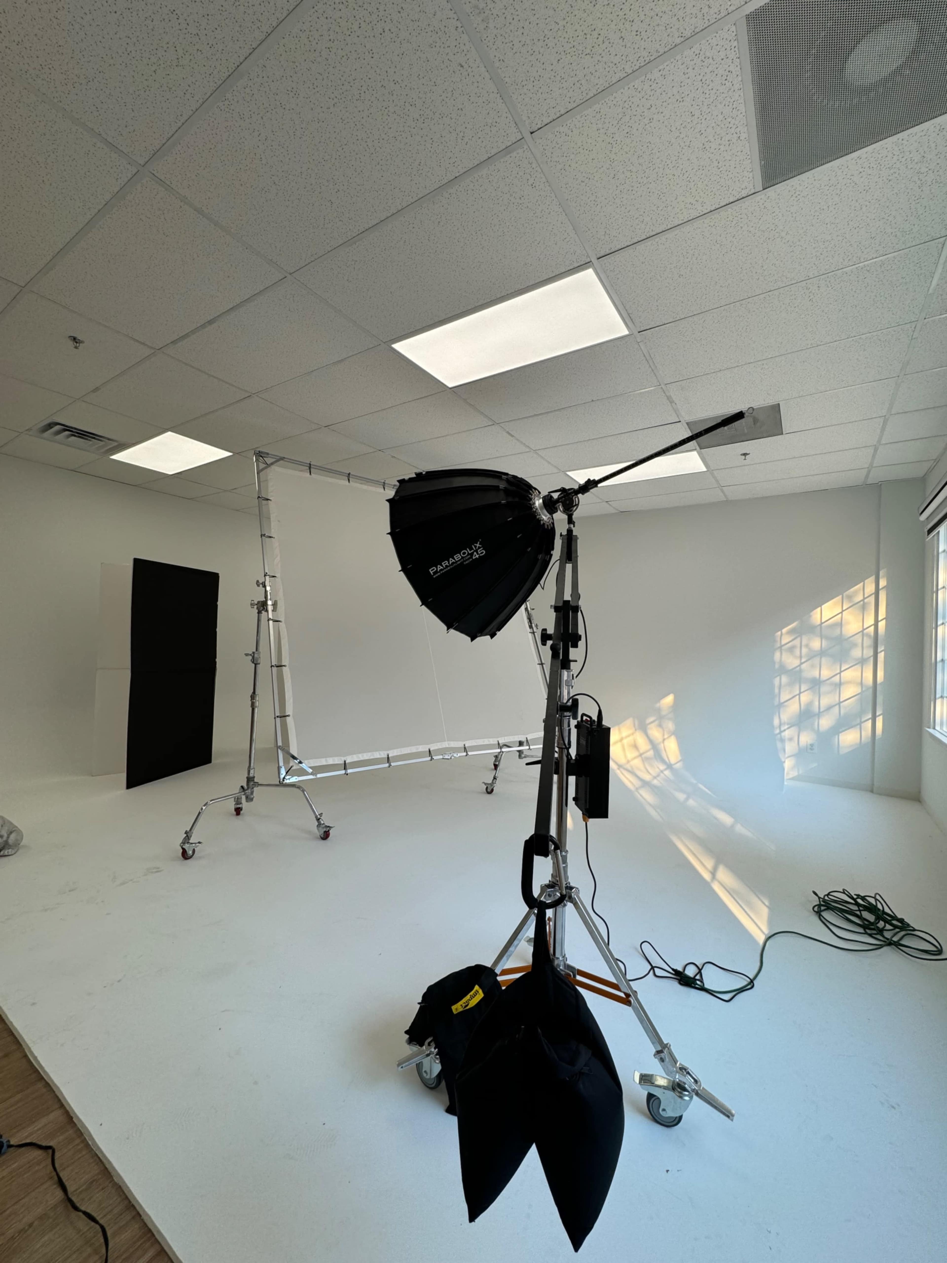 A photography studio is set up with a lighting umbrella, a backdrop frame, and various cables on the floor.