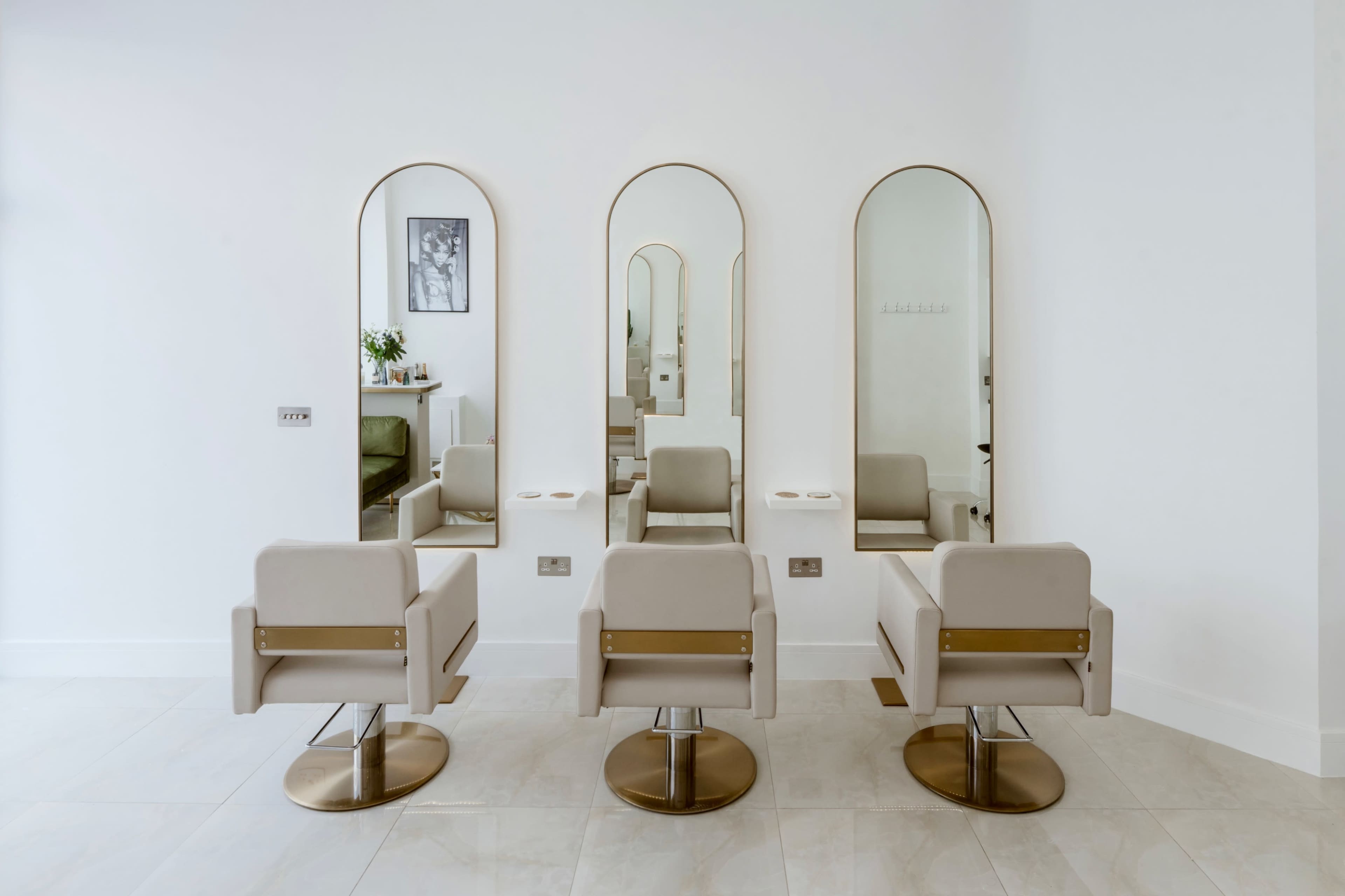 The image shows a modern hair salon interior with three styling chairs and arched mirrors arranged against a white wall.