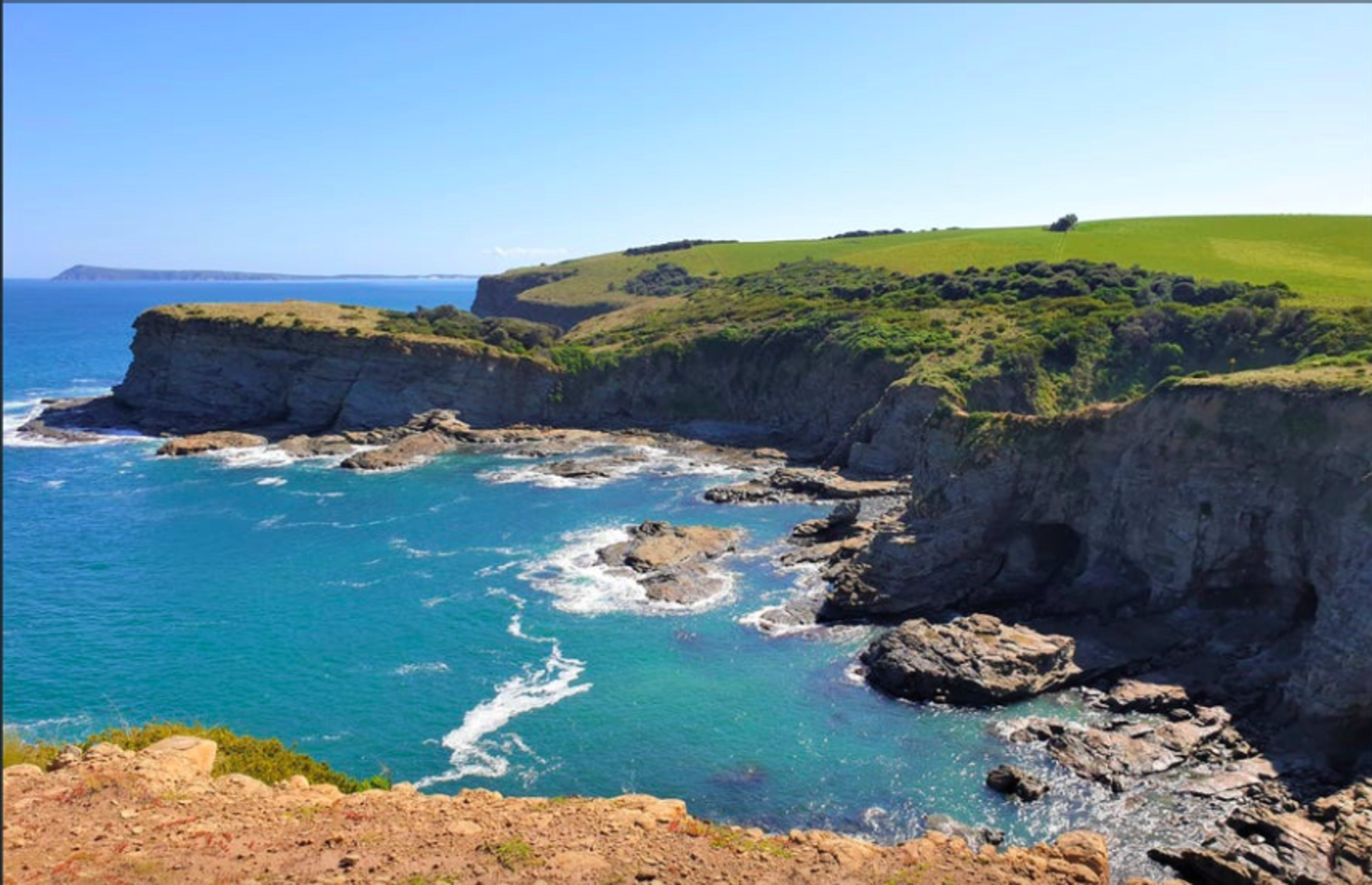 A coastline features rocky cliffs and clear blue waters, with green hills rising in the background.