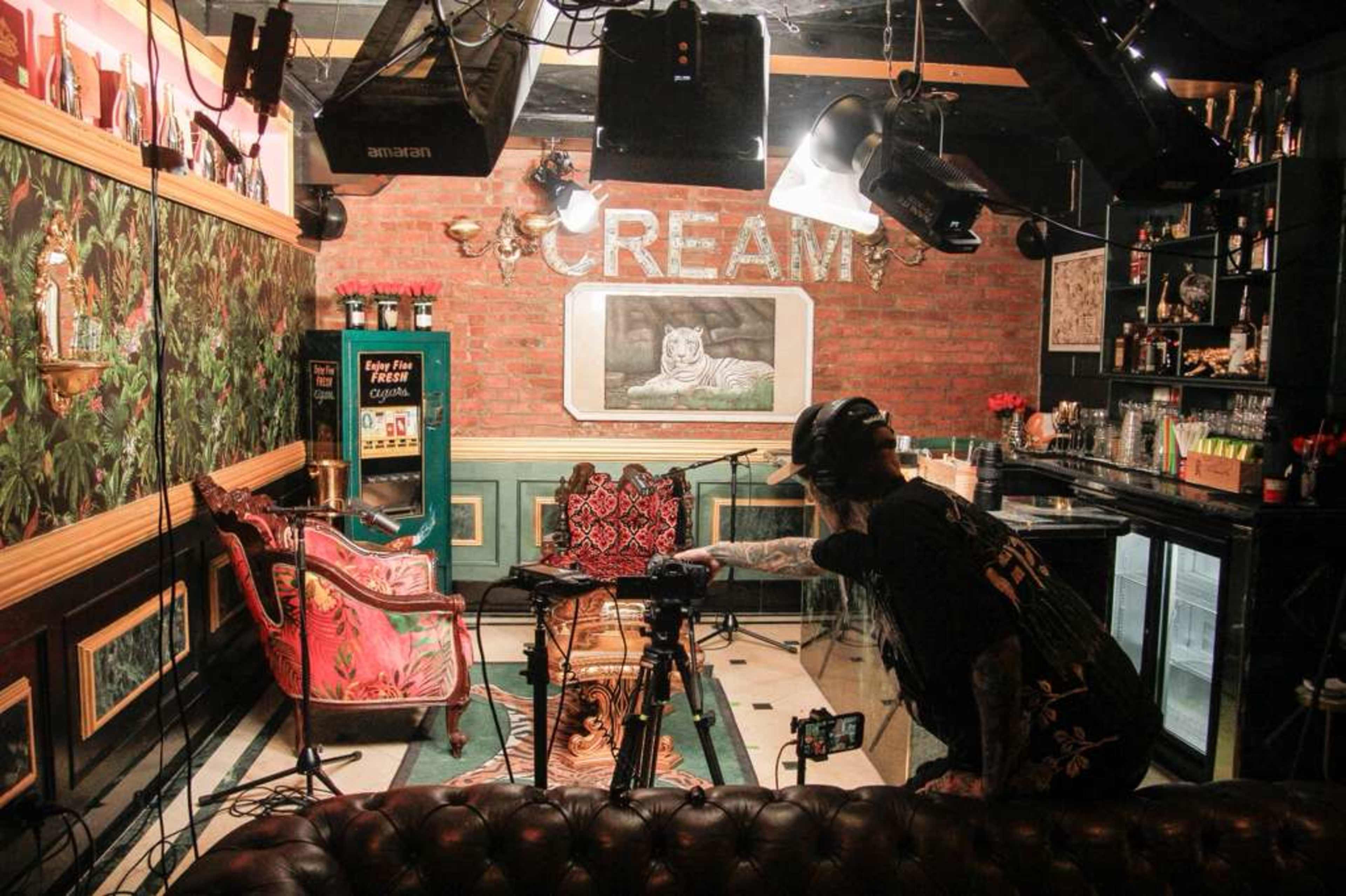 A person is adjusting equipment in a stylish indoor setup featuring a vintage chair, bar area, and decorative wall art.