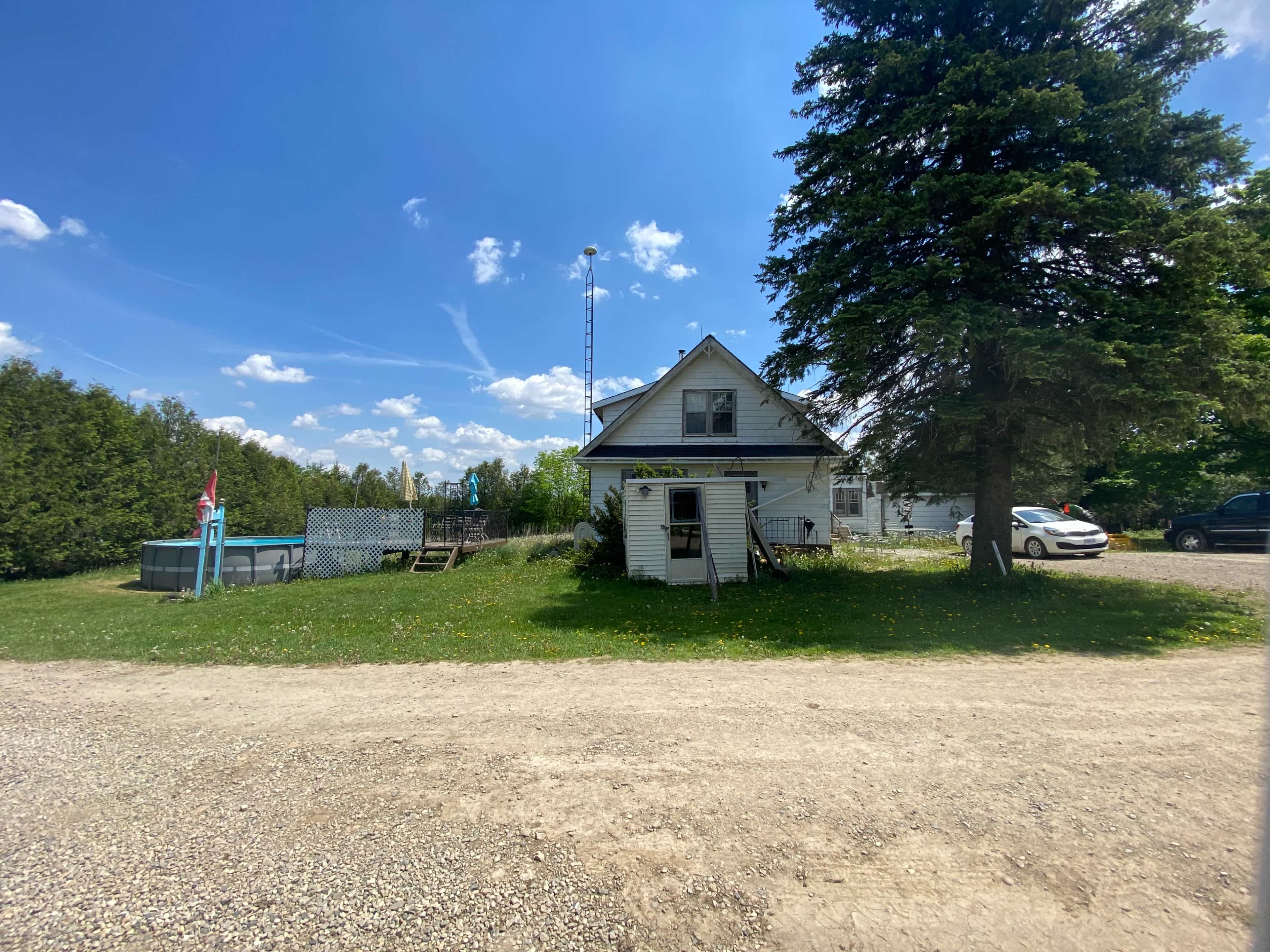 A two-story white house is situated near a driveway, with a swimming pool and a flag in the yard.
