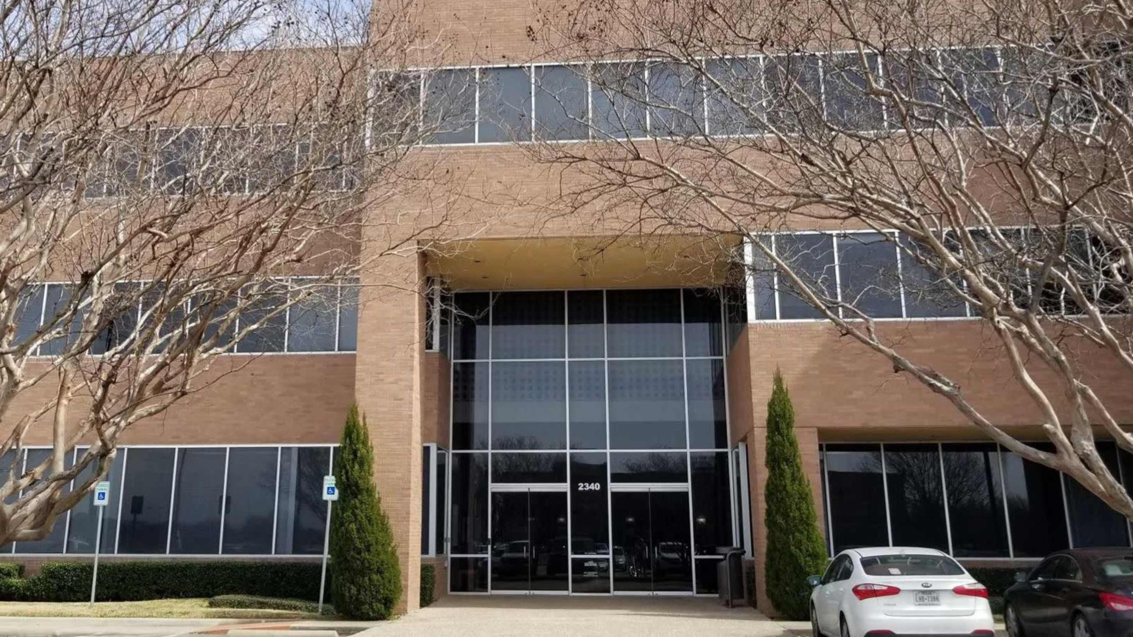 A four-story brick office building with large glass windows and two symmetrical trees flanking the entrance.