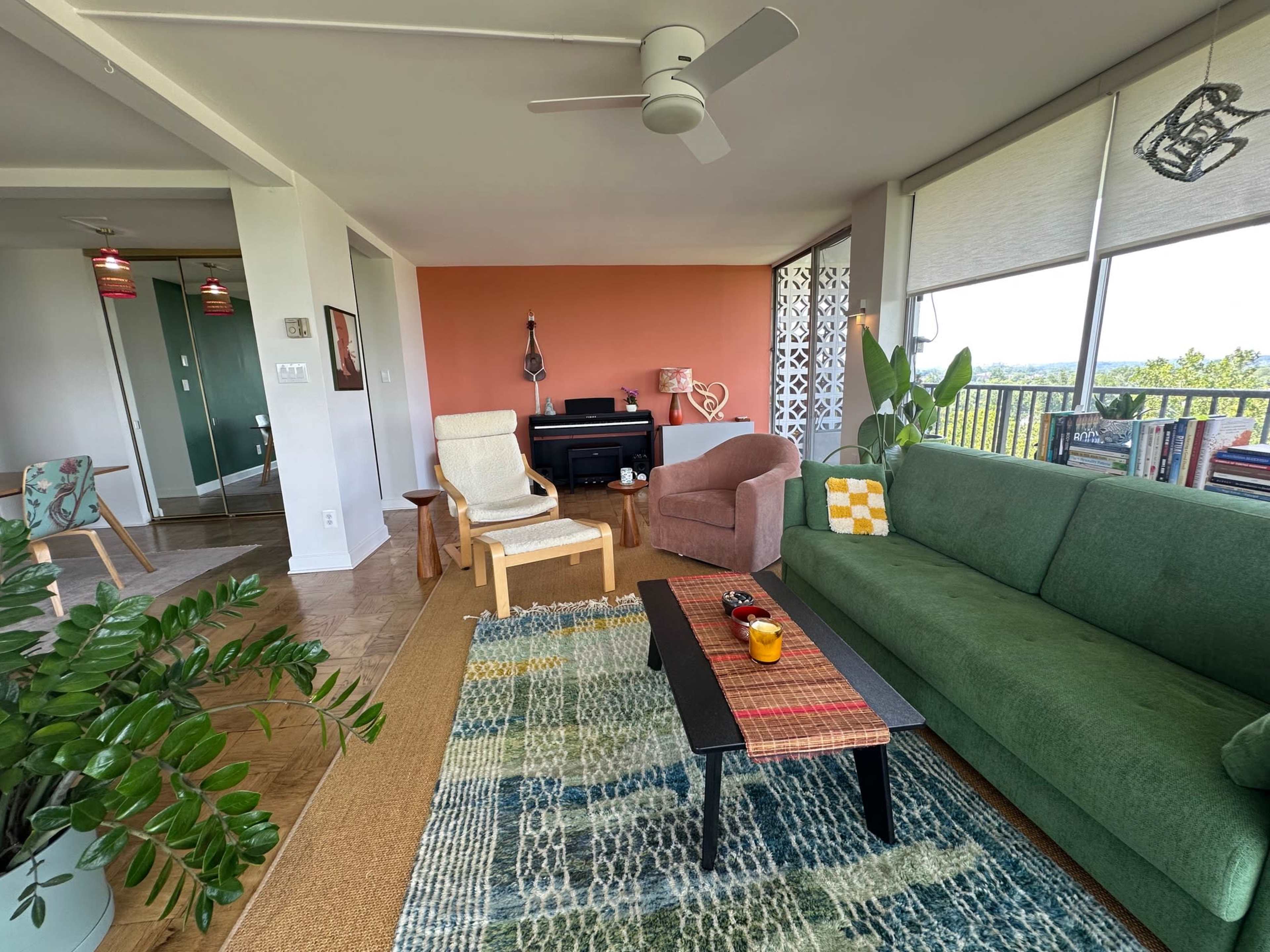 A modern living room features a green sofa, a patterned rug, a wooden coffee table, and a view of the outdoors through large windows.