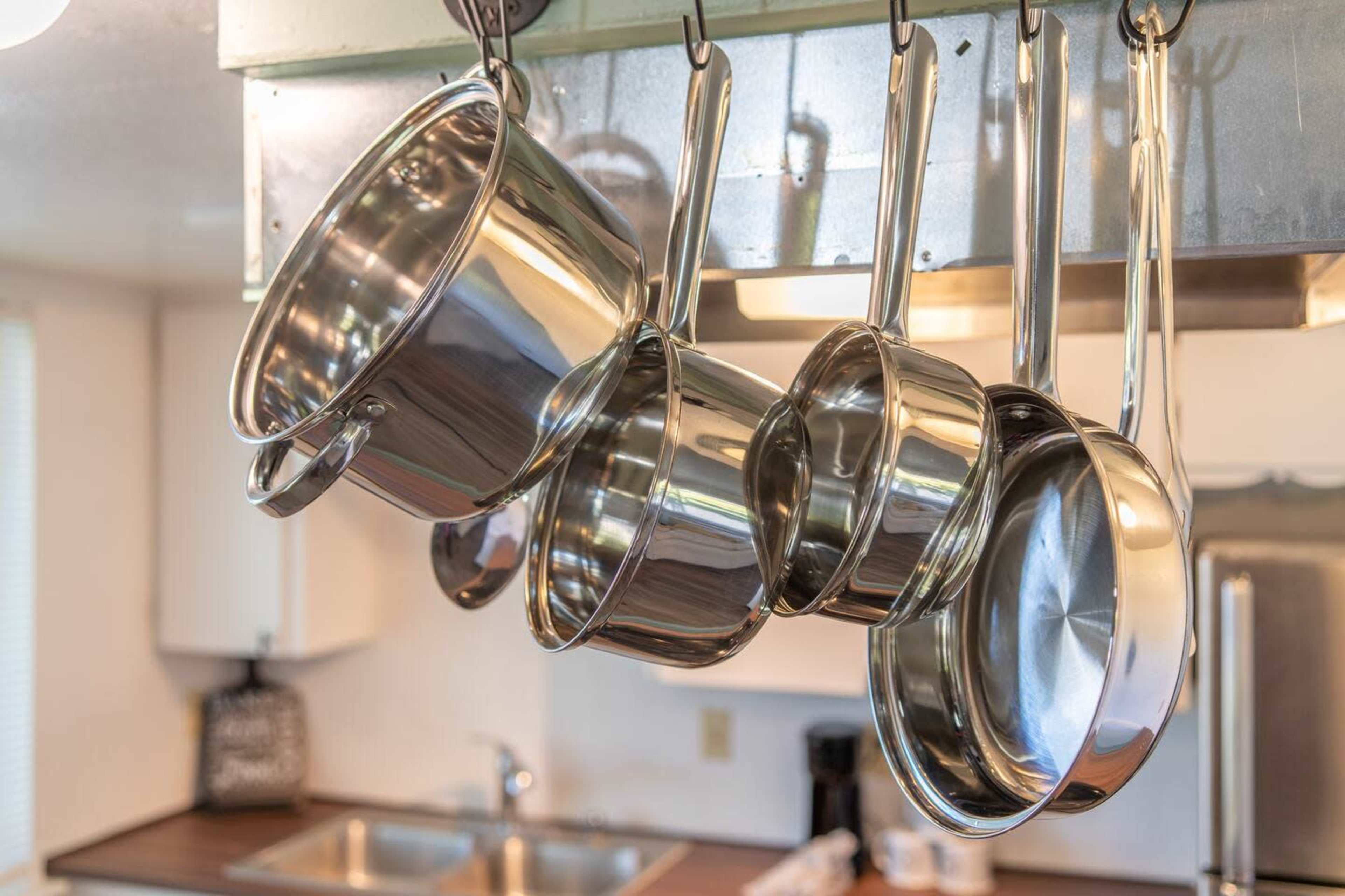 A set of stainless steel pots and pans hang from a rack in a kitchen.