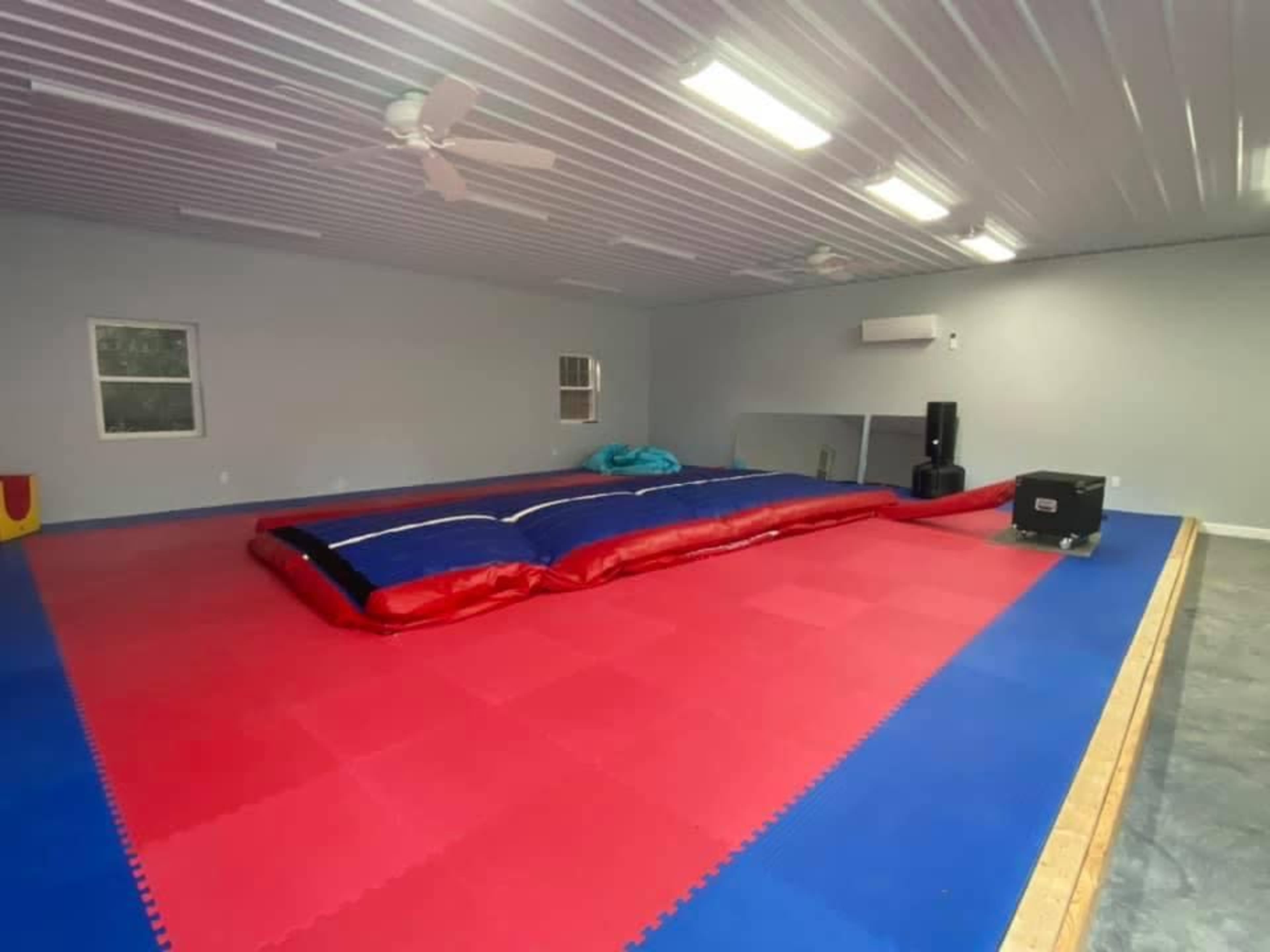 A large indoor gymnasium with a red and blue gymnastics mat, a foam pit, and some equipment along the walls.