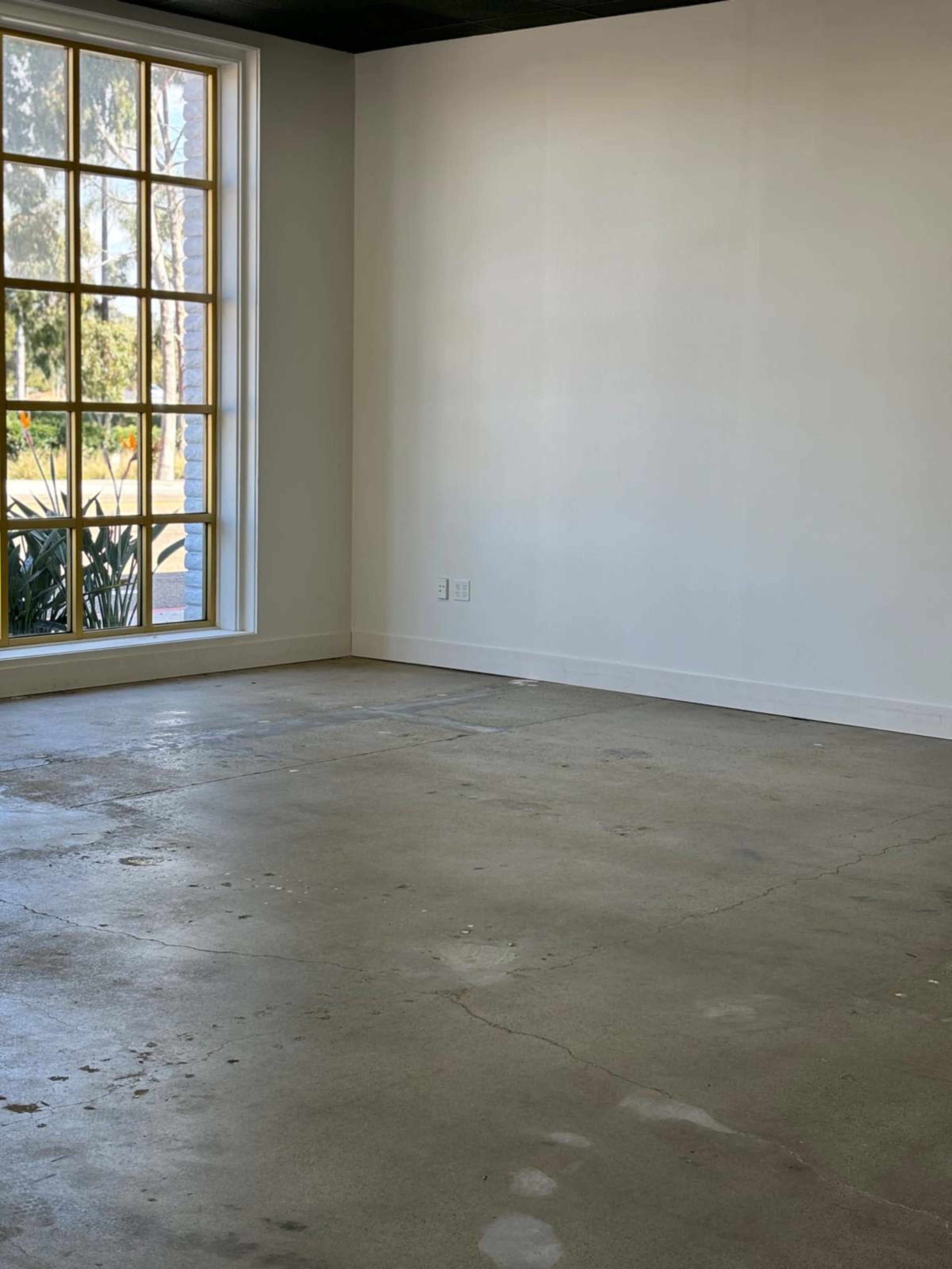 The image shows an empty room with a concrete floor and a large window on one wall.