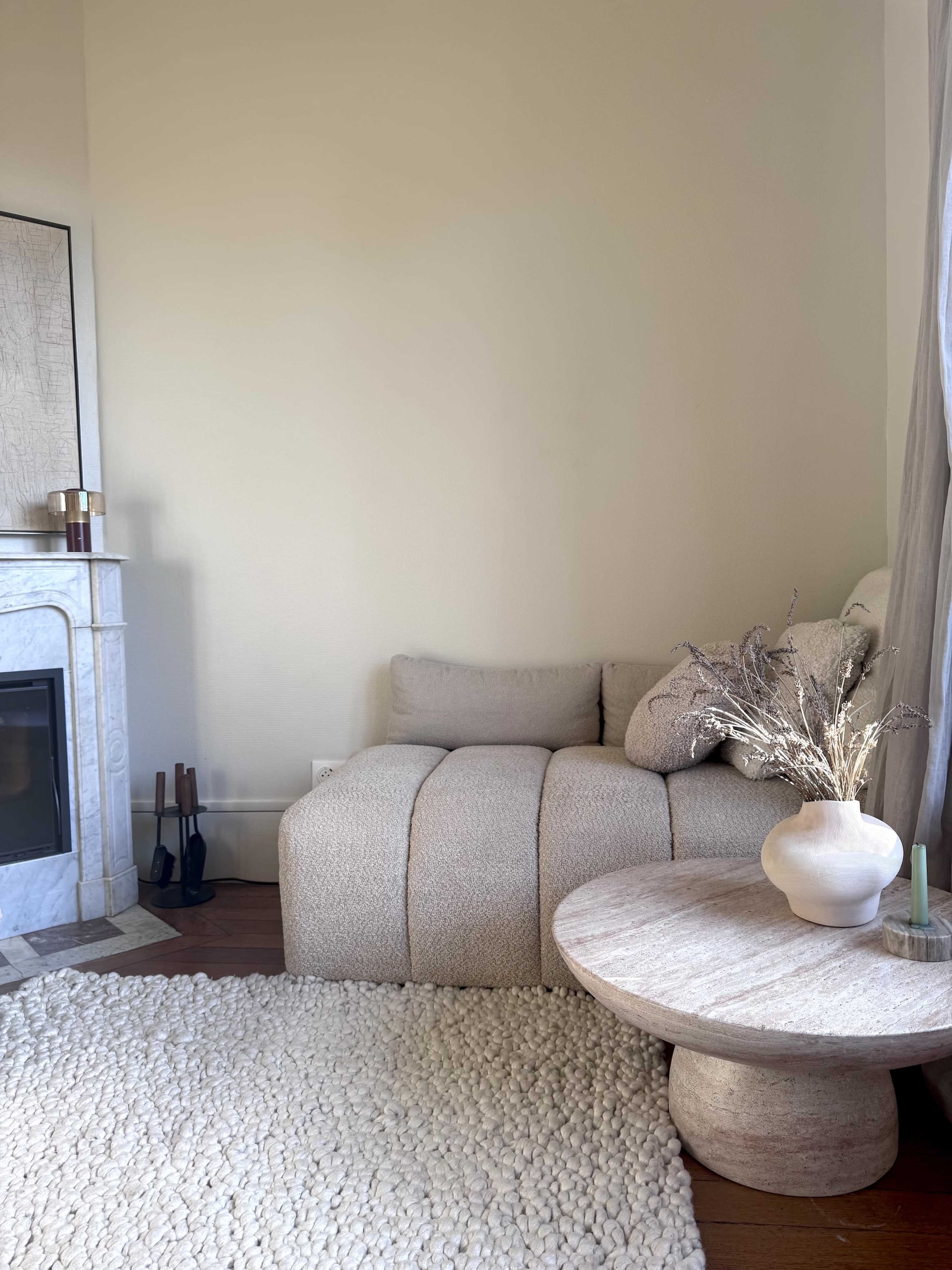 A cozy living room corner features a textured light-colored sofa, a round coffee table, a soft area rug, and a small decorative vase with dried flowers.