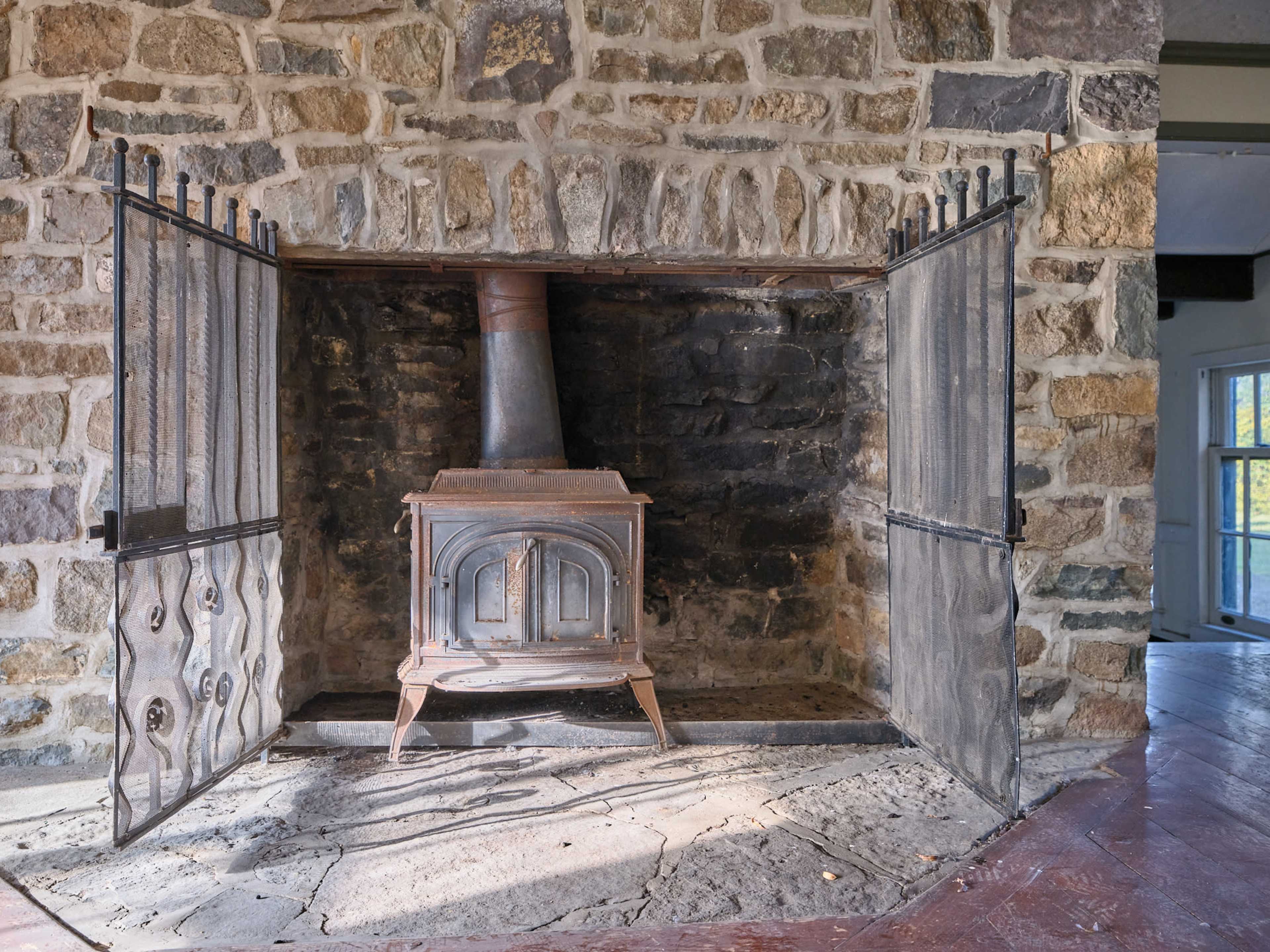 A stone fireplace with an ironwood stove and hinged doors, set in a rustic interior.