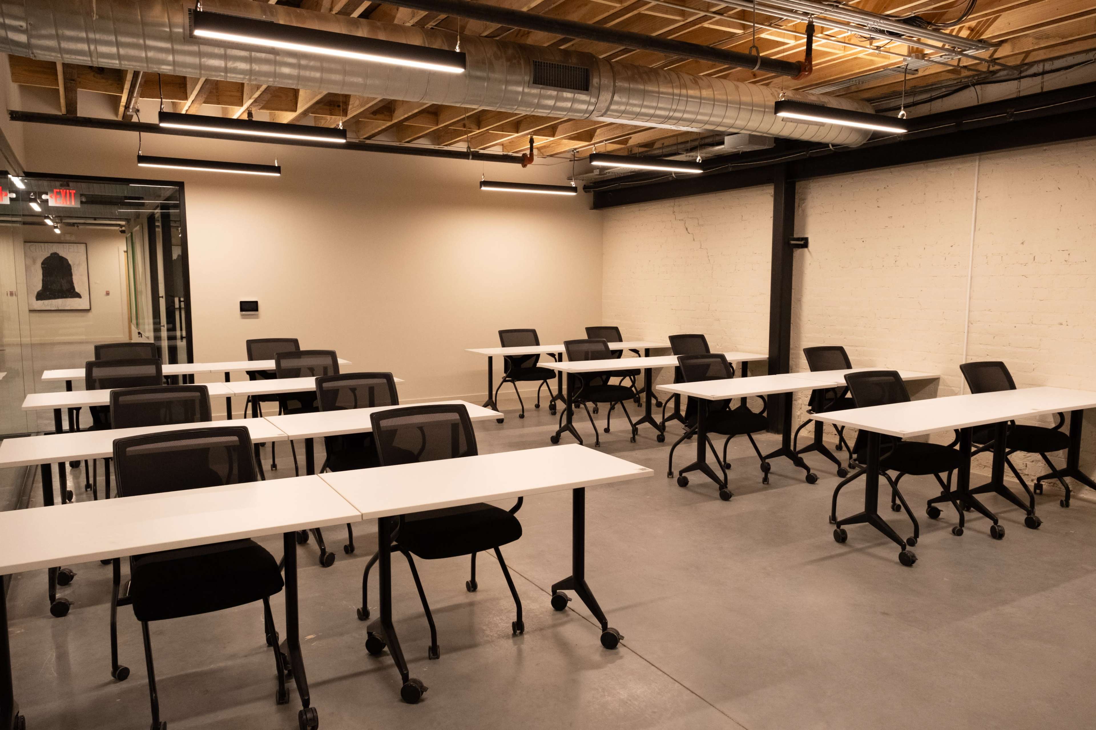 A conference room with multiple white tables and black chairs arranged in a grid pattern against a light-colored wall.