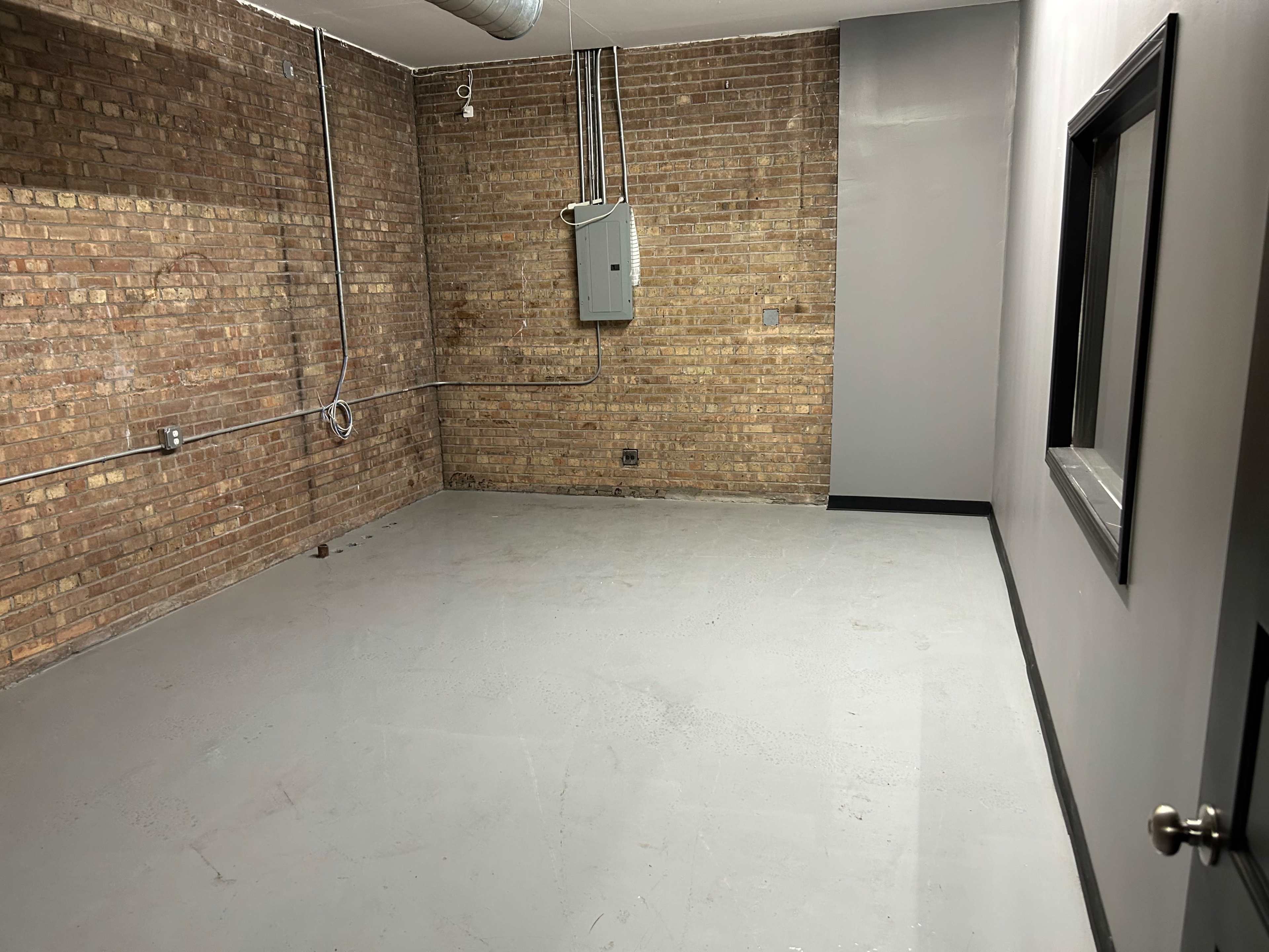 An empty room with bare brick walls, a gray floor, and an electrical panel mounted on one wall.