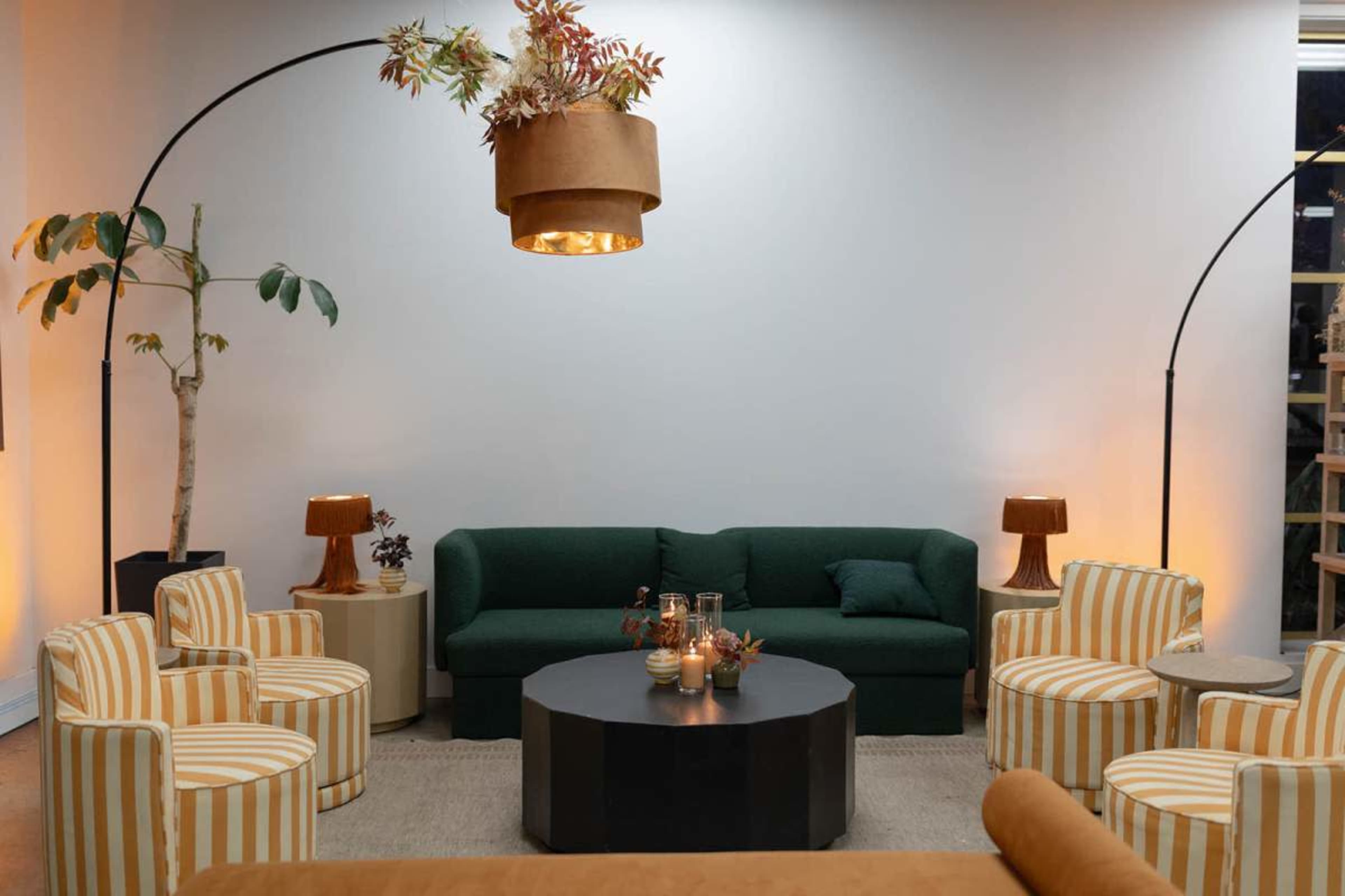 The image shows a modern lounge area featuring a green sofa, striped chairs, a round black coffee table, and decorative plants under soft lighting.