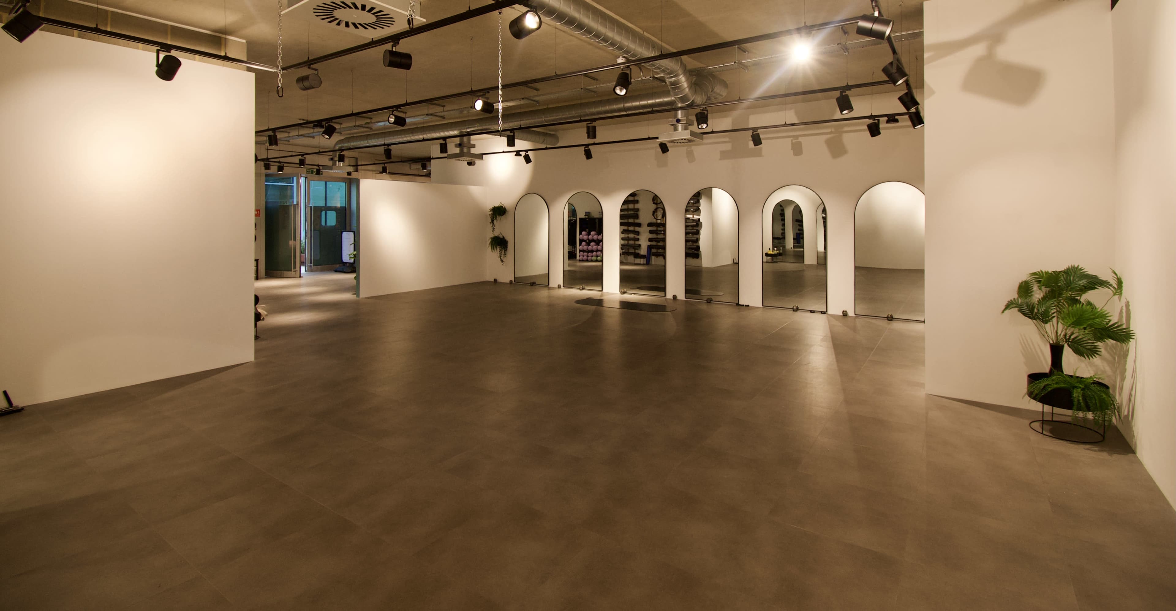 The image shows an empty, well-lit gallery or exhibition space with smooth gray flooring and arched doorways along one wall.