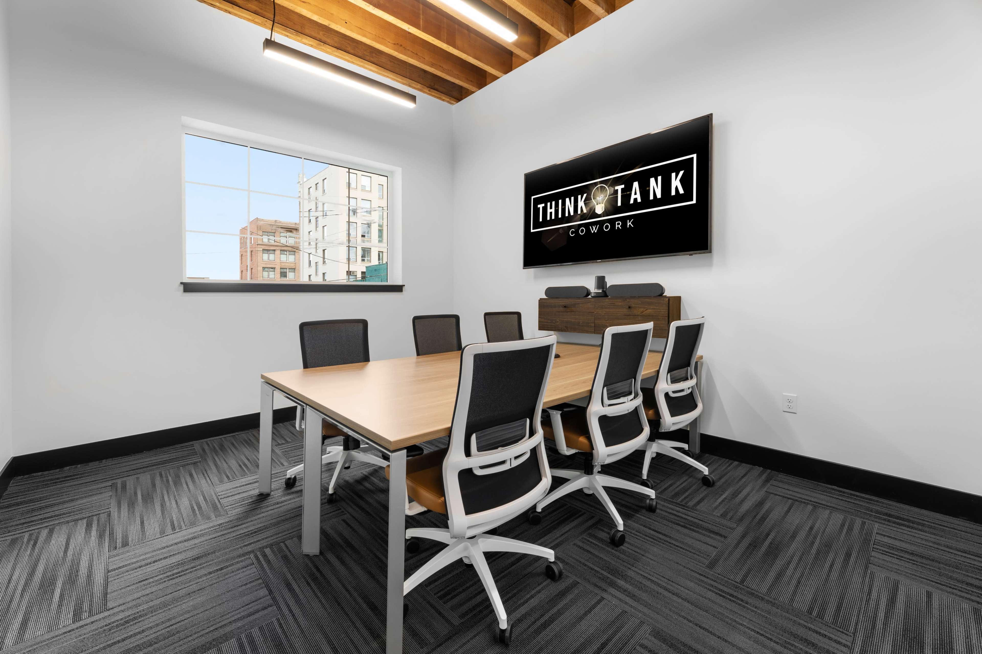 A modern conference room features a long wooden table surrounded by white chairs, with a large screen displaying the "THINK TANK COWORK" logo on the wall.