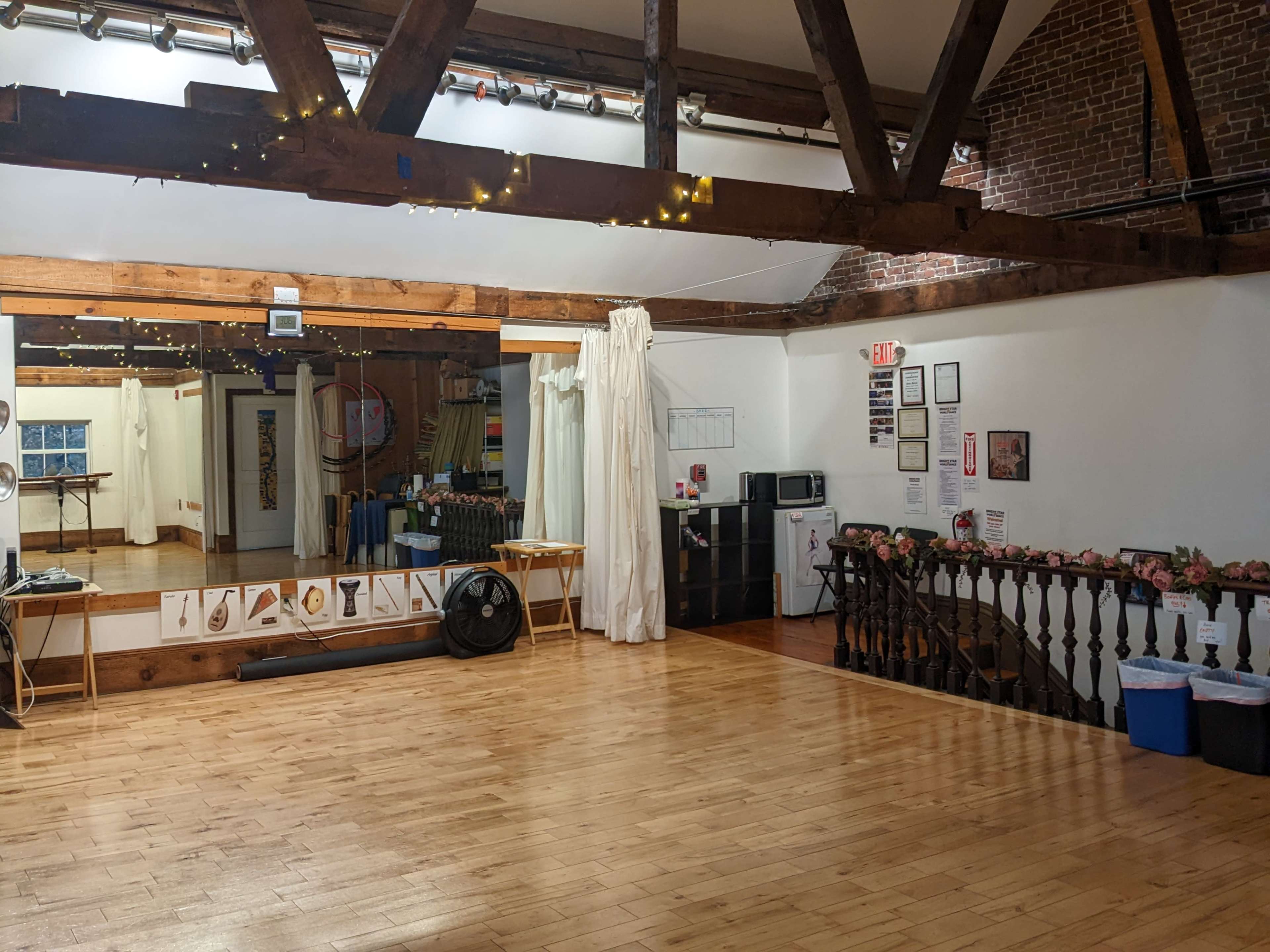 A spacious dance studio with a wooden floor, exposed beams, and various exercise equipment arranged along one wall.