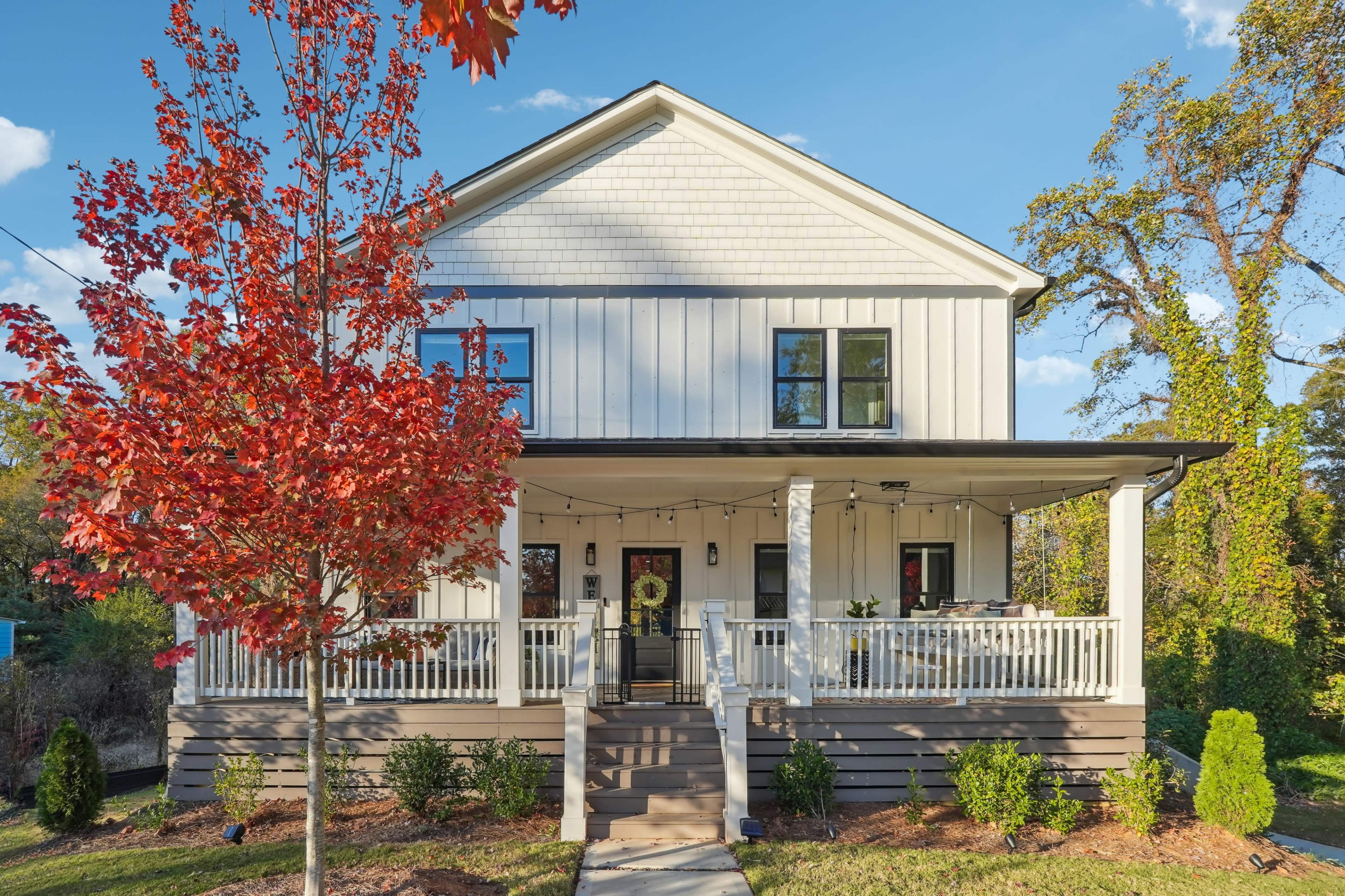 A modern two-story house with a white exterior, a front porch, and a red maple tree in the foreground.