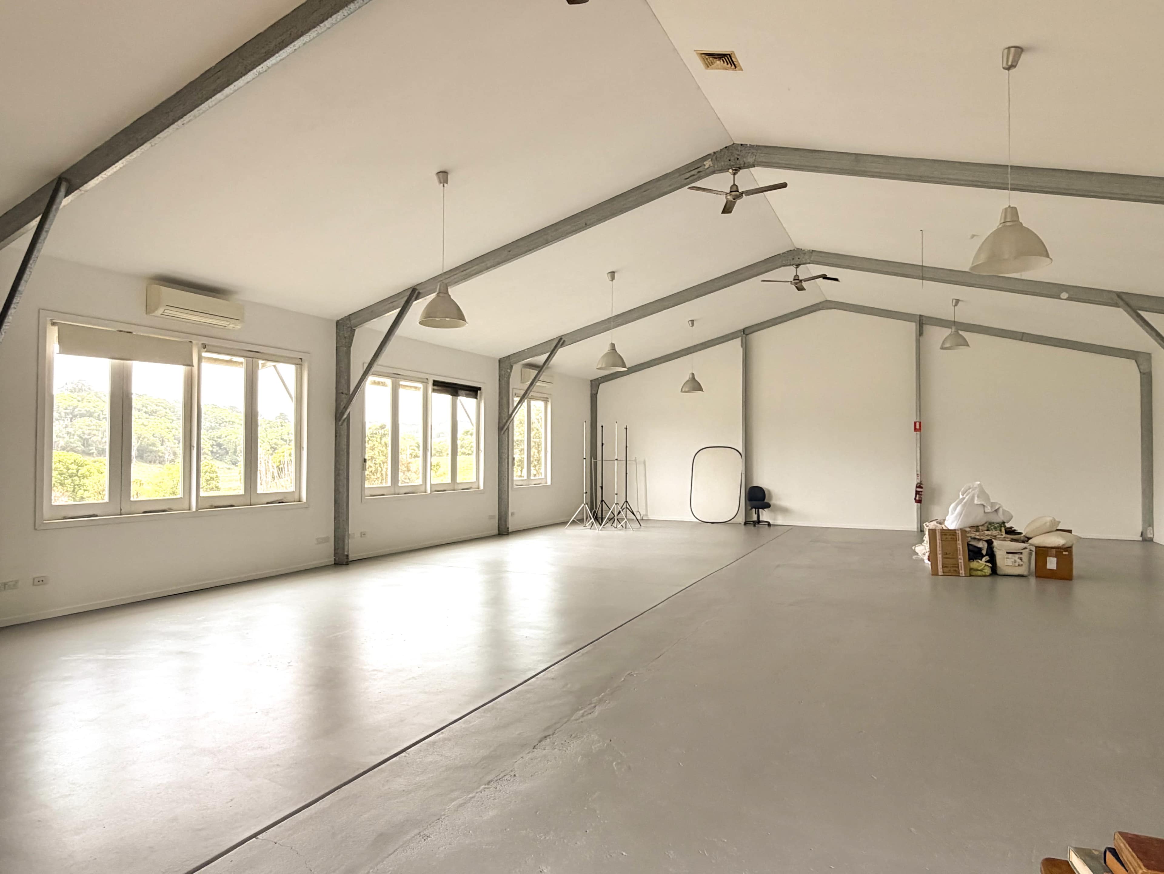 A large, empty room with high ceilings, windows on one side, and a concrete floor is visible.