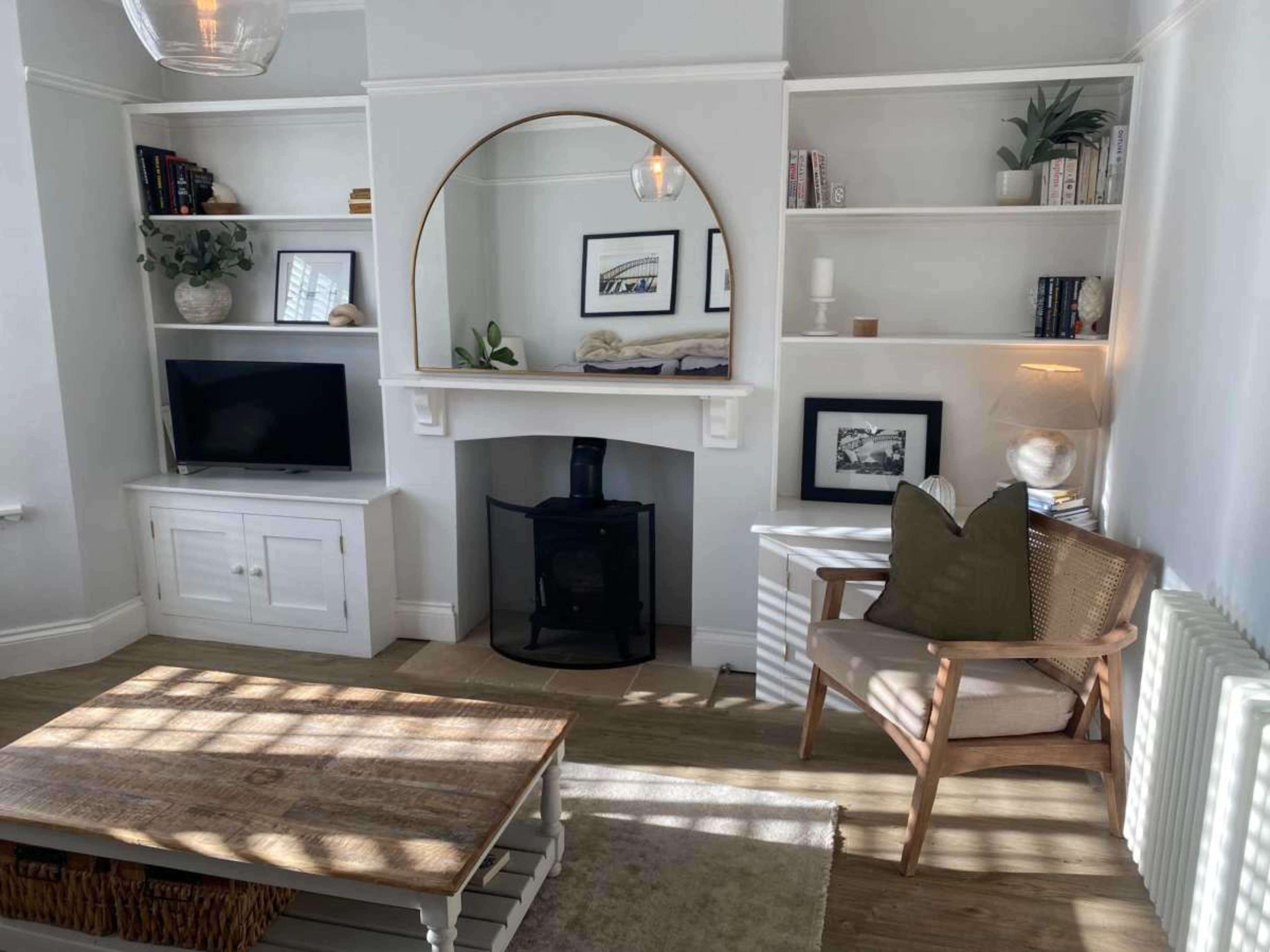 The image shows a cozy living room featuring a modern design with built-in shelves, a fireplace, a TV cabinet, and a comfortable chair placed beside a wooden coffee table.