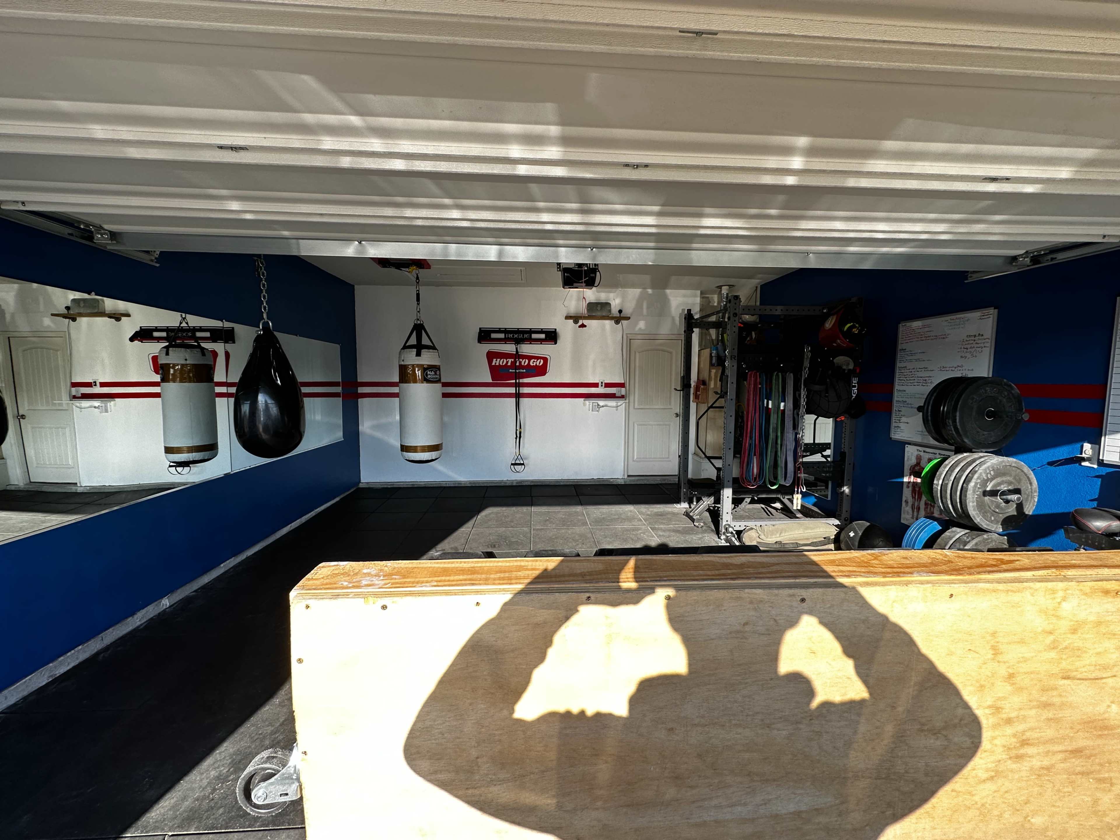 A home gym with boxing bags, weights, and exercise equipment arranged against blue and white walls.