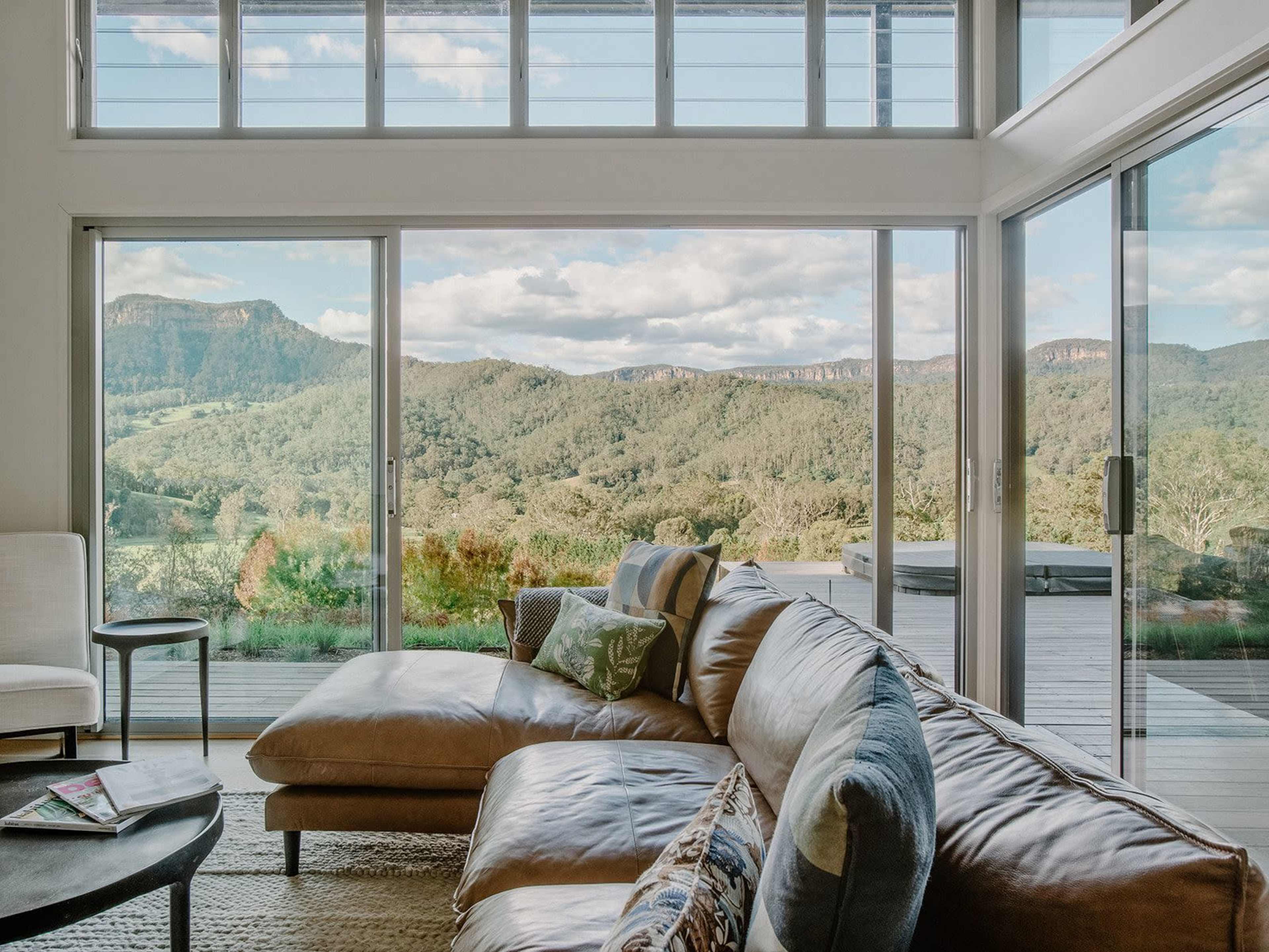 A modern living room features a large sectional sofa and expansive windows that provide a view of rolling hills and mountains in the distance.