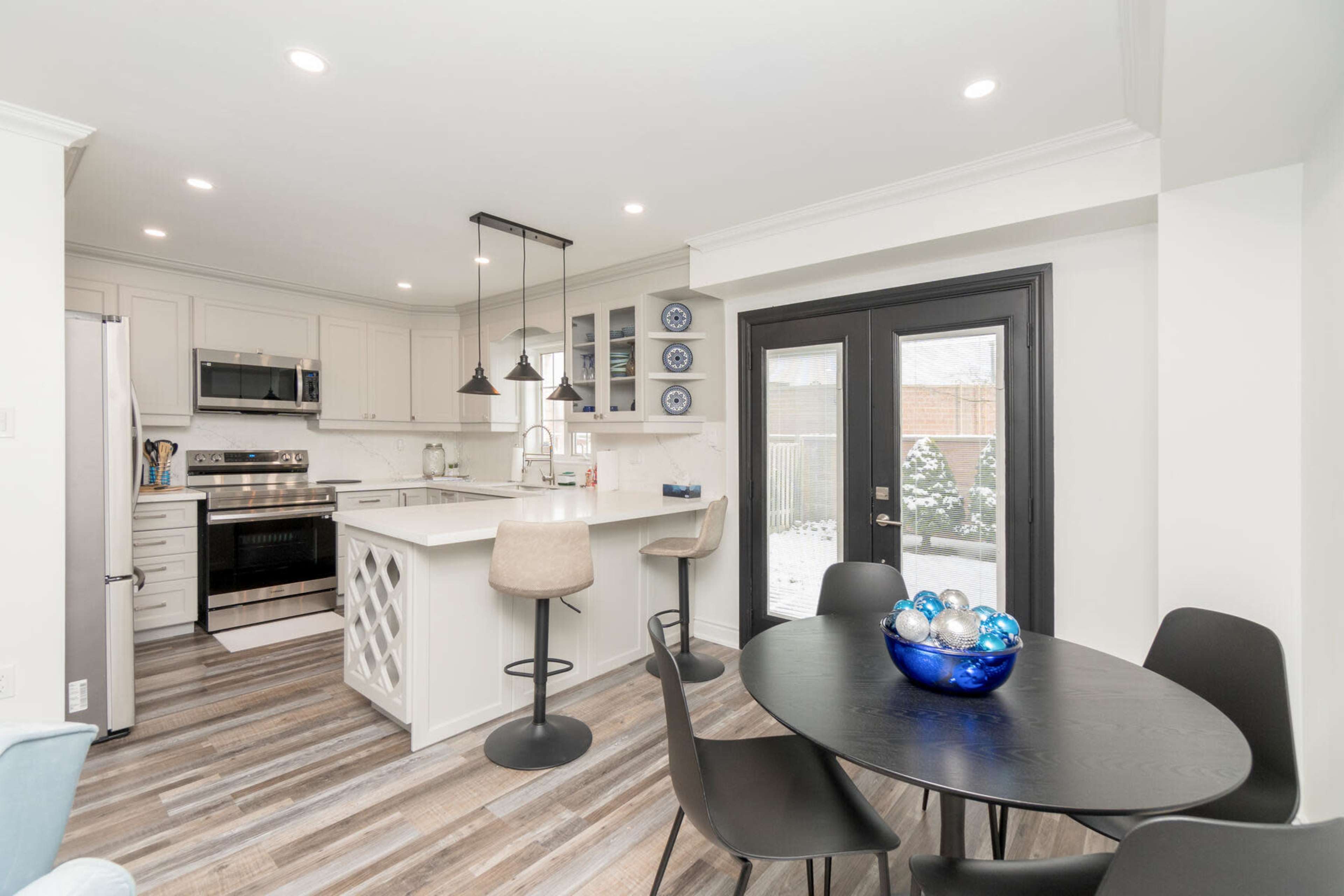 A modern kitchen with stainless steel appliances, a central island, and a dining area featuring a round table with a blue glass bowl.