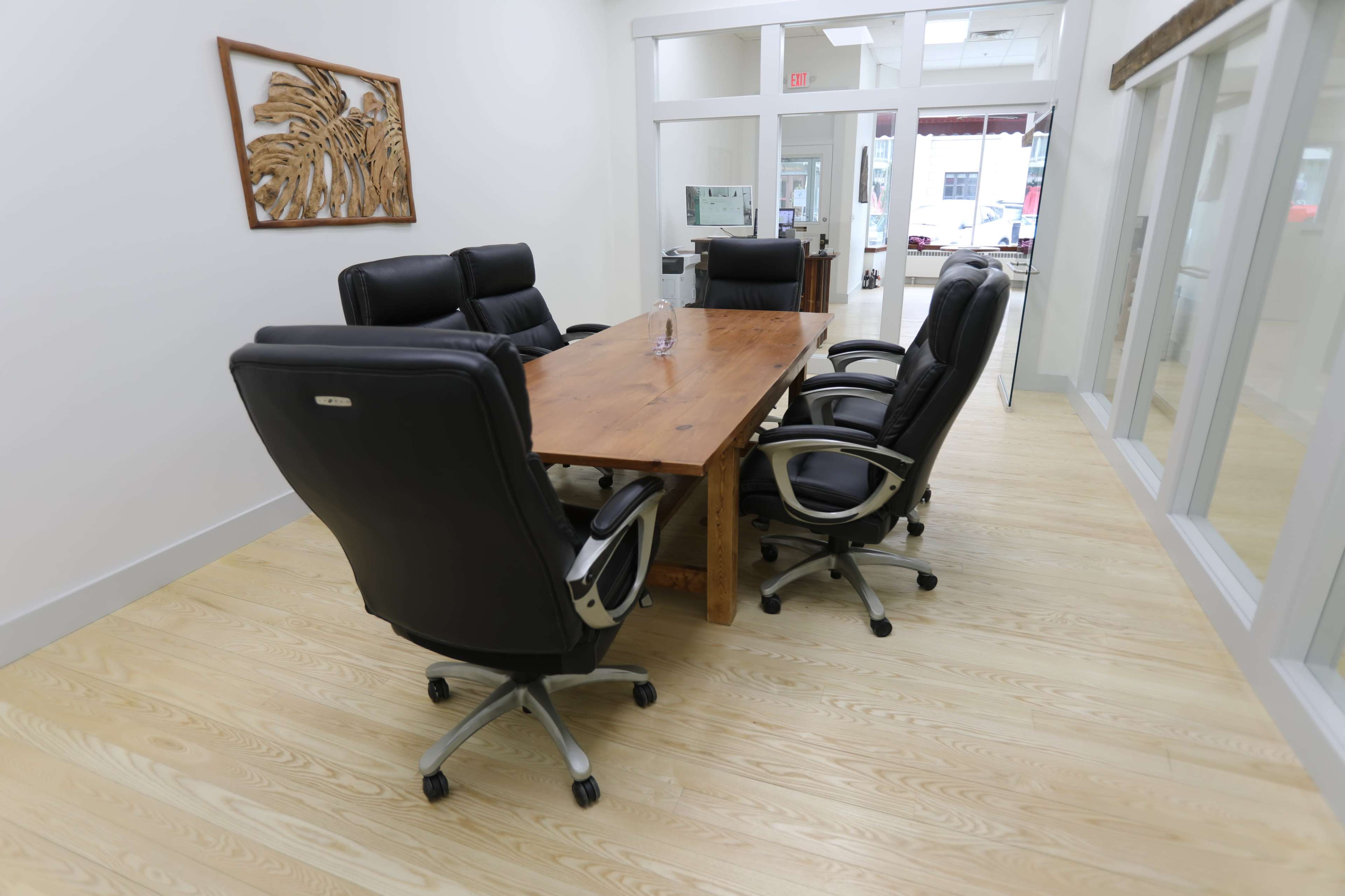 A modern conference room features a wooden table surrounded by four black office chairs.