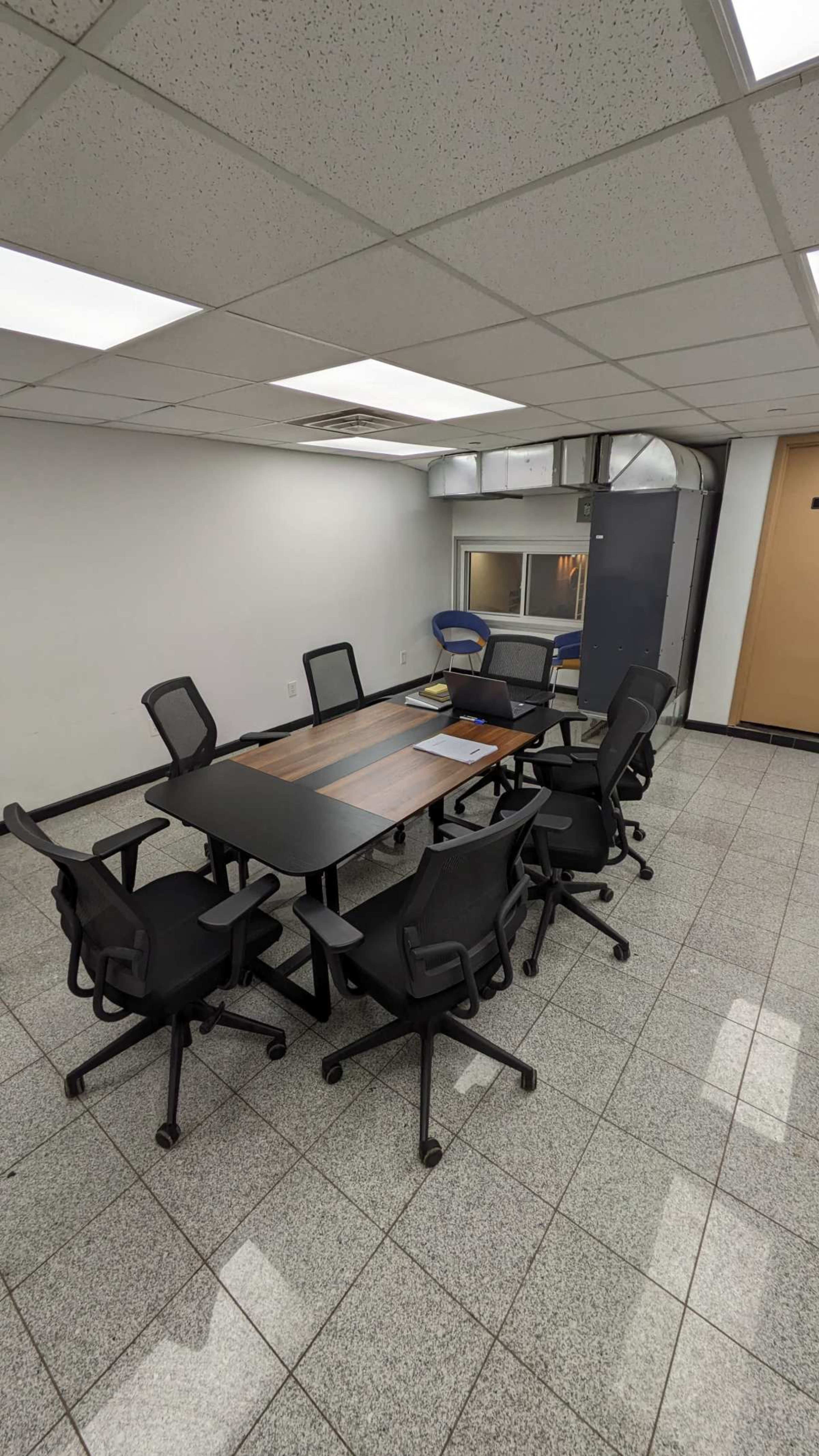 A conference room features a rectangular table surrounded by several rolling black chairs on a tiled floor.