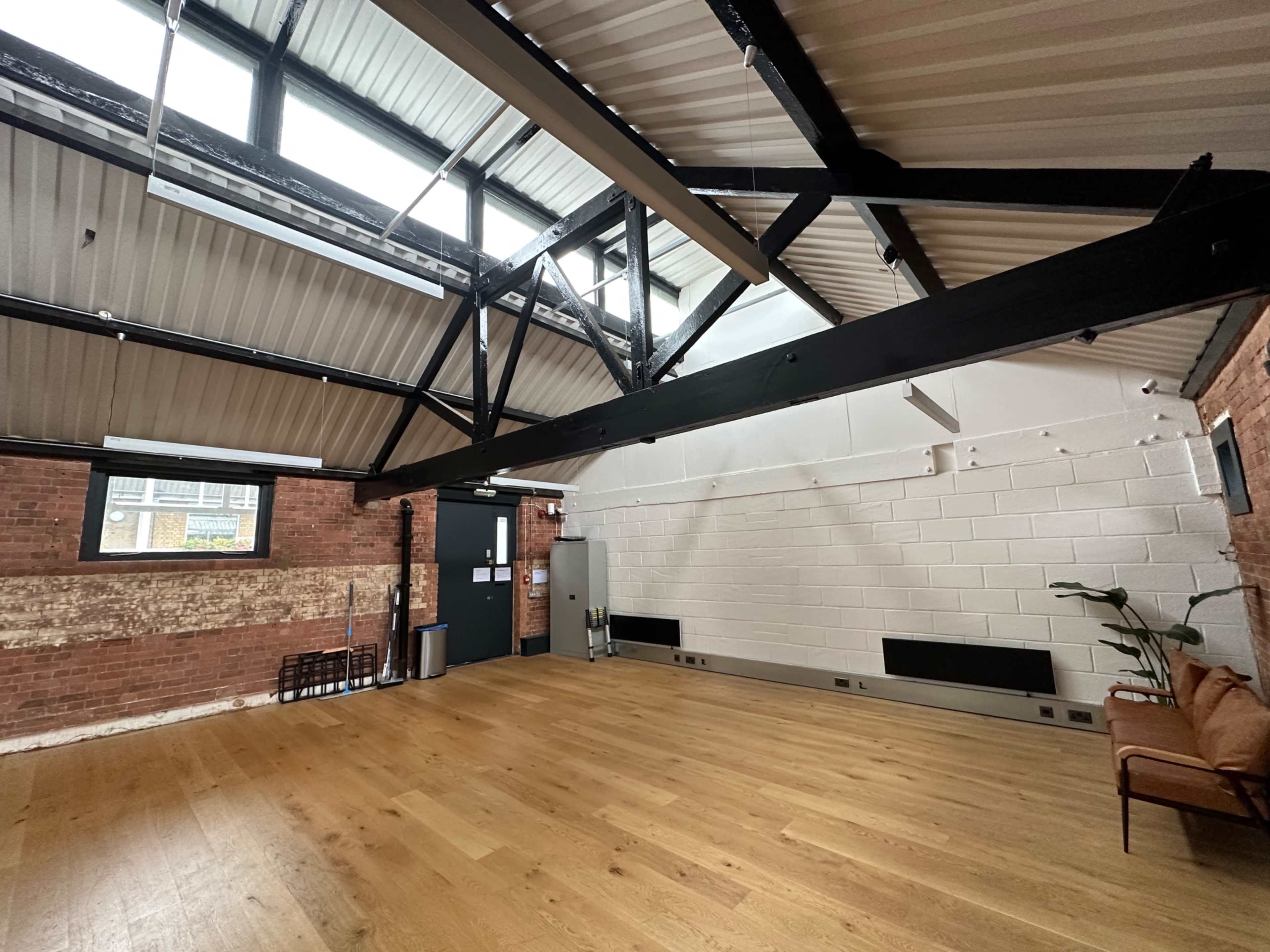 A spacious interior with high ceilings, exposed beams, wood flooring, and a sofa against the wall.