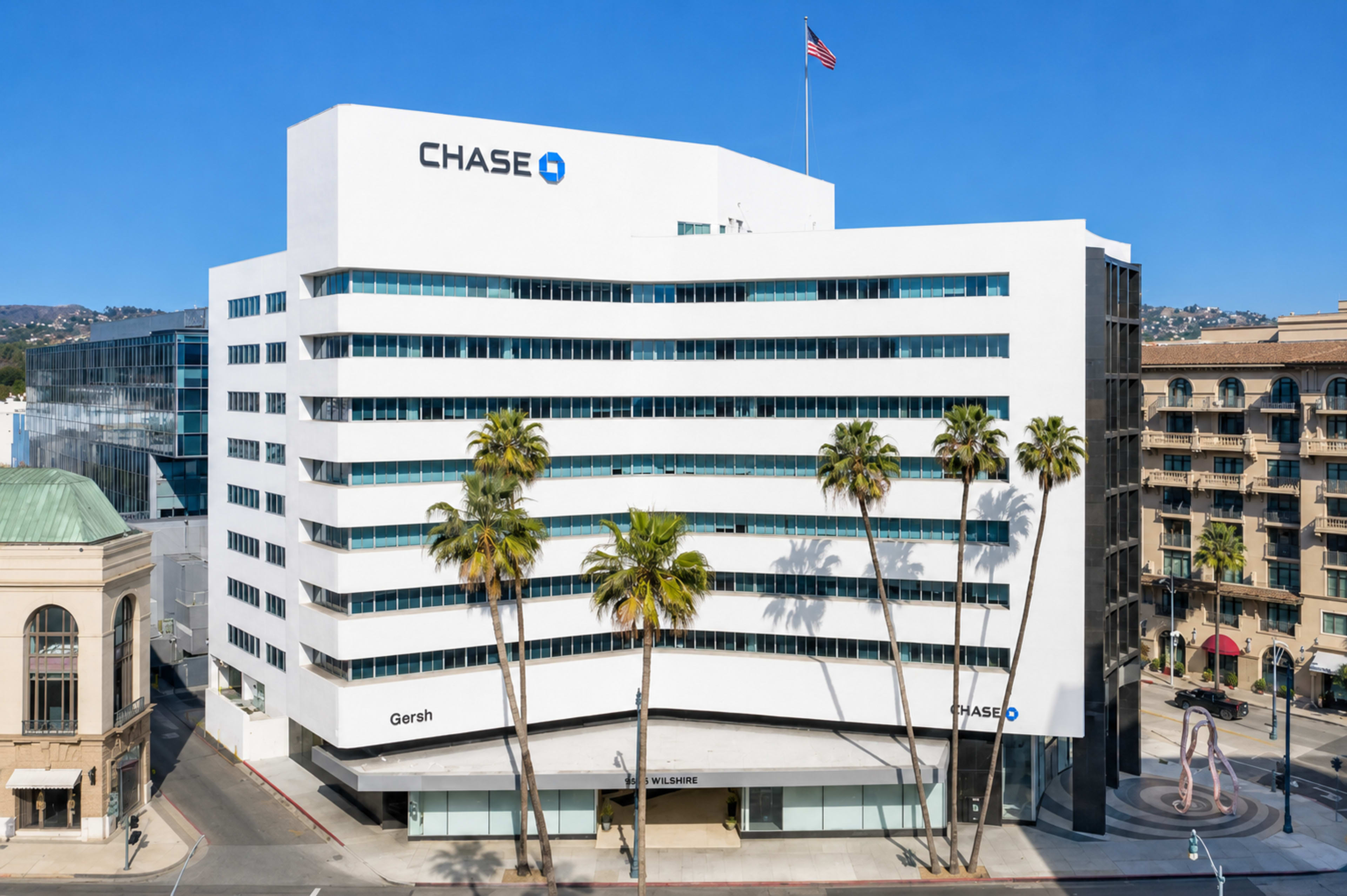 The image shows a modern, multi-story building with the Chase logo prominently displayed on the top, surrounded by palm trees and located at the corner of a city street.