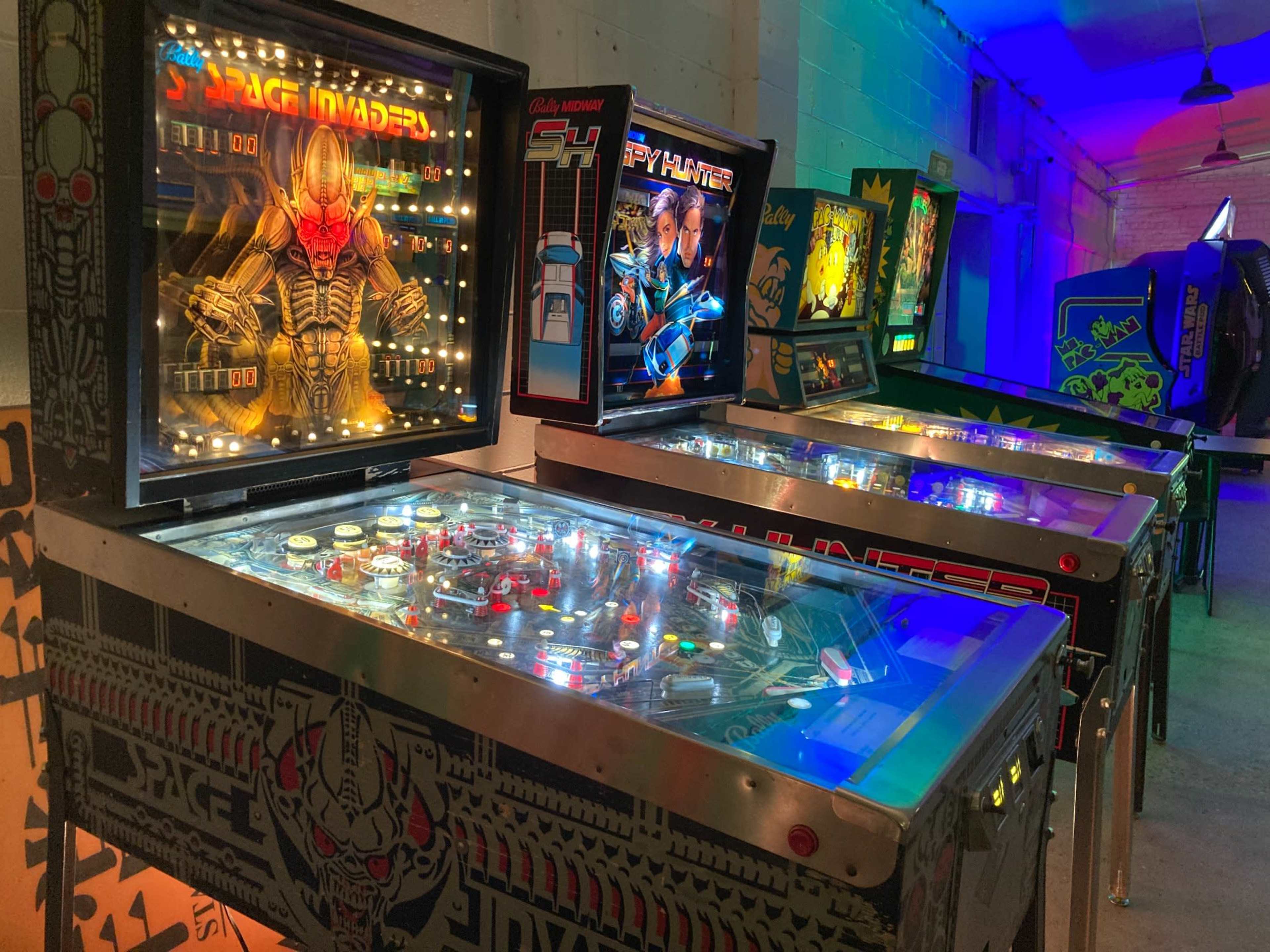 A row of vintage pinball machines in a brightly lit arcade.