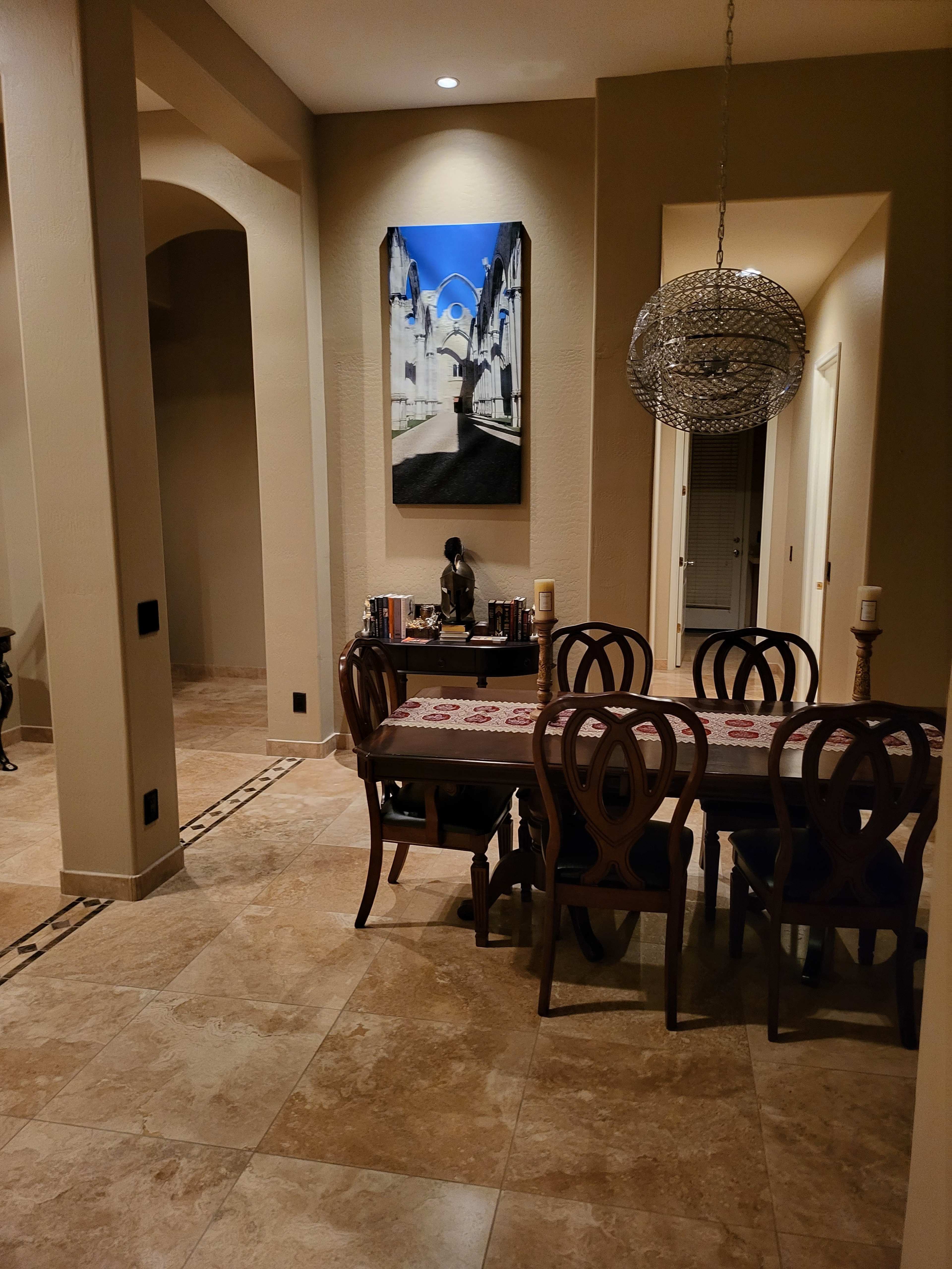 A dining area with a wooden table and chairs is visible, featuring a wall art piece and a hallway leading to other rooms.