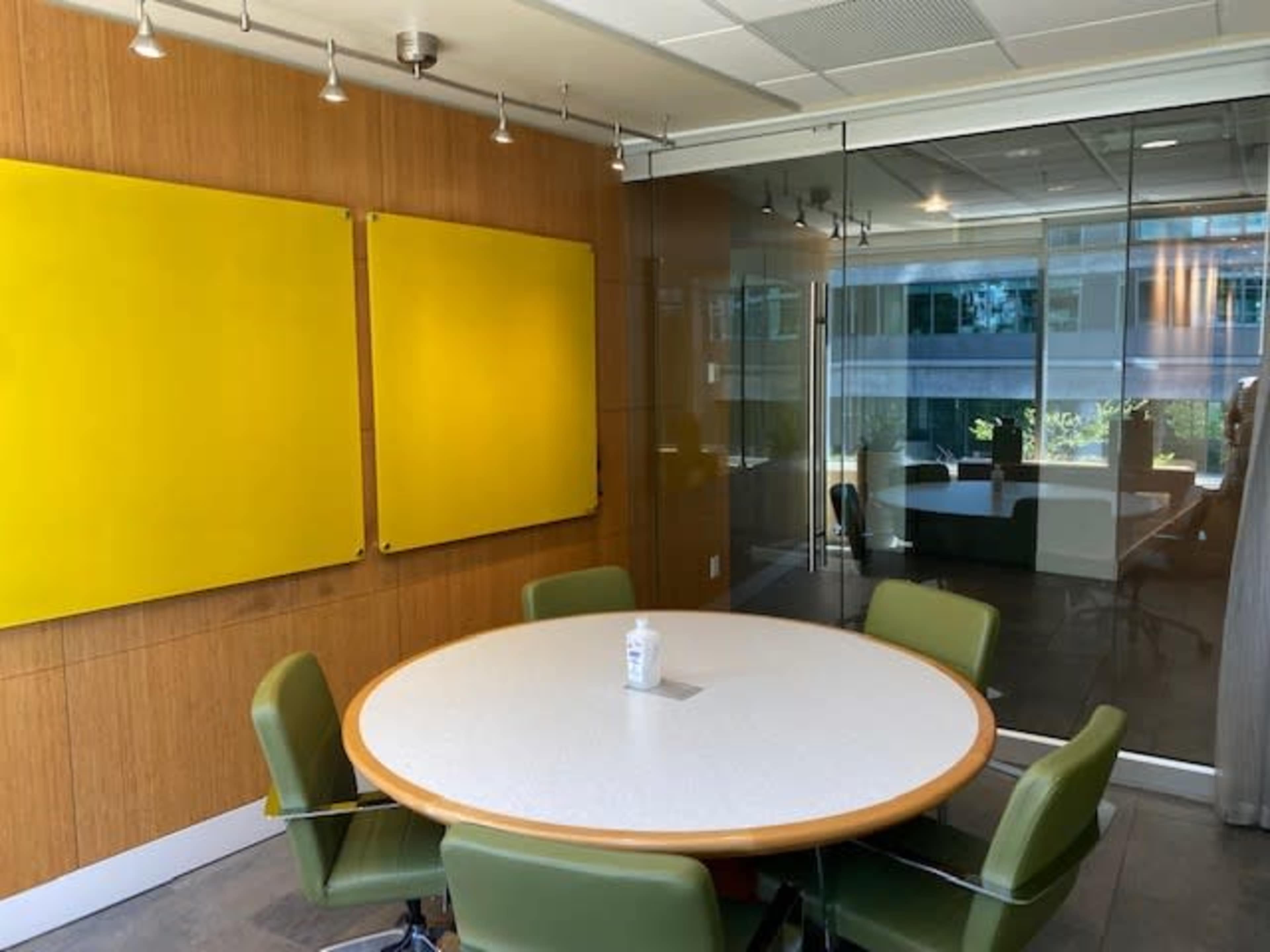 A modern conference room with a round table and green chairs, flanked by two large yellow wall panels.