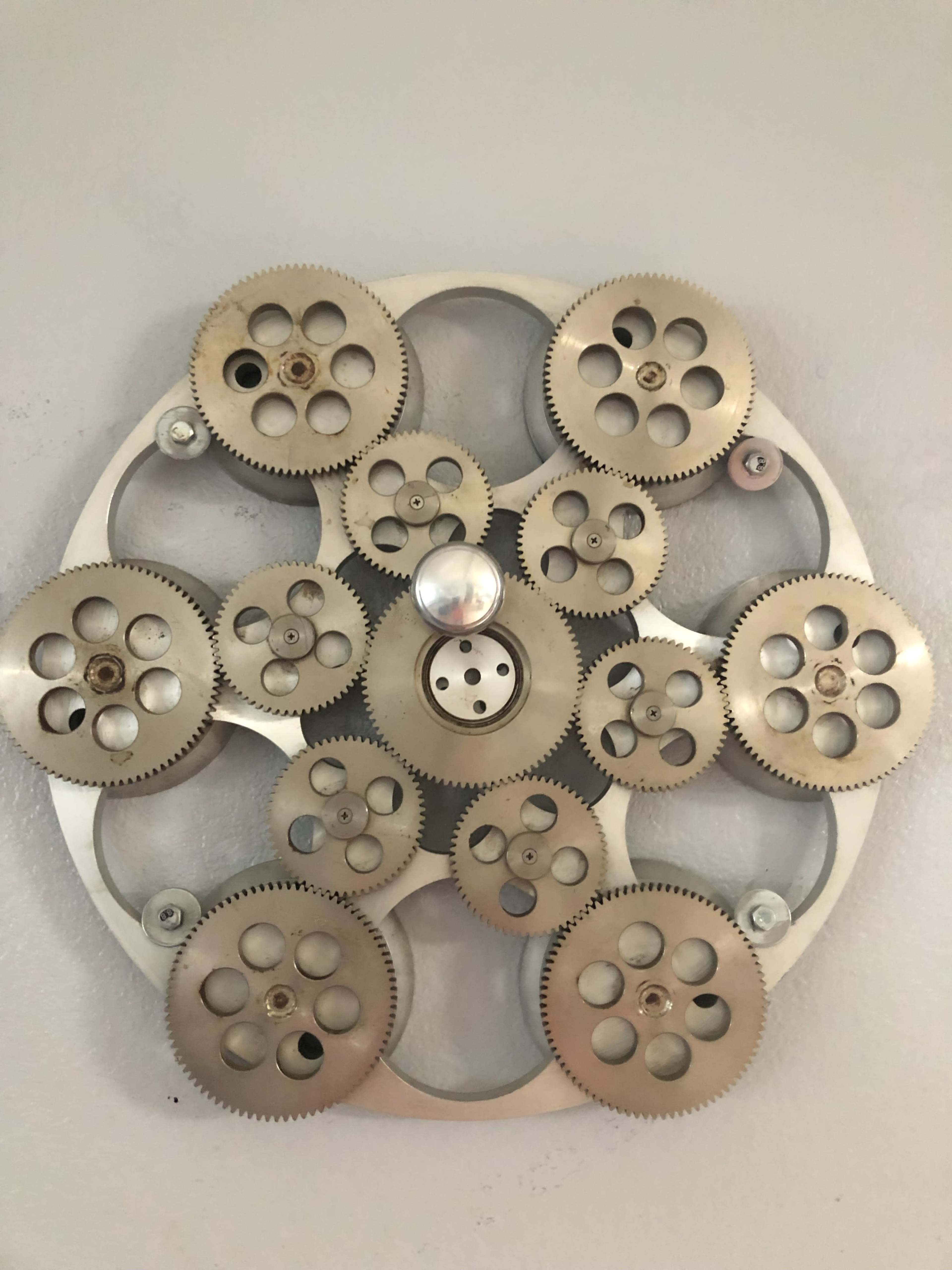 A circular arrangement of metal gears with varying sizes and teeth is mounted on a wall.