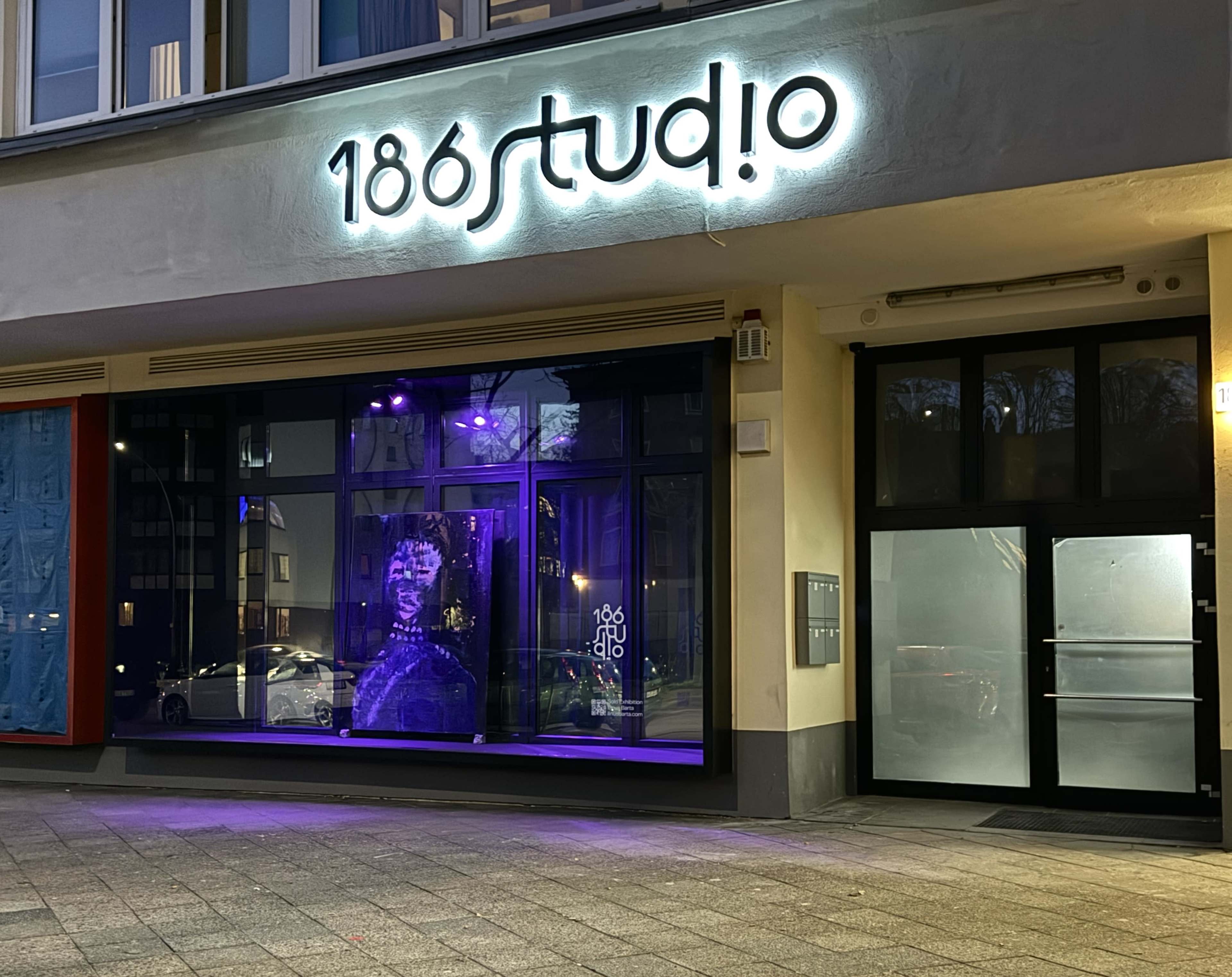 The image shows the exterior of a studio named "186studio," featuring a large illuminated sign and a window display with purple lighting.