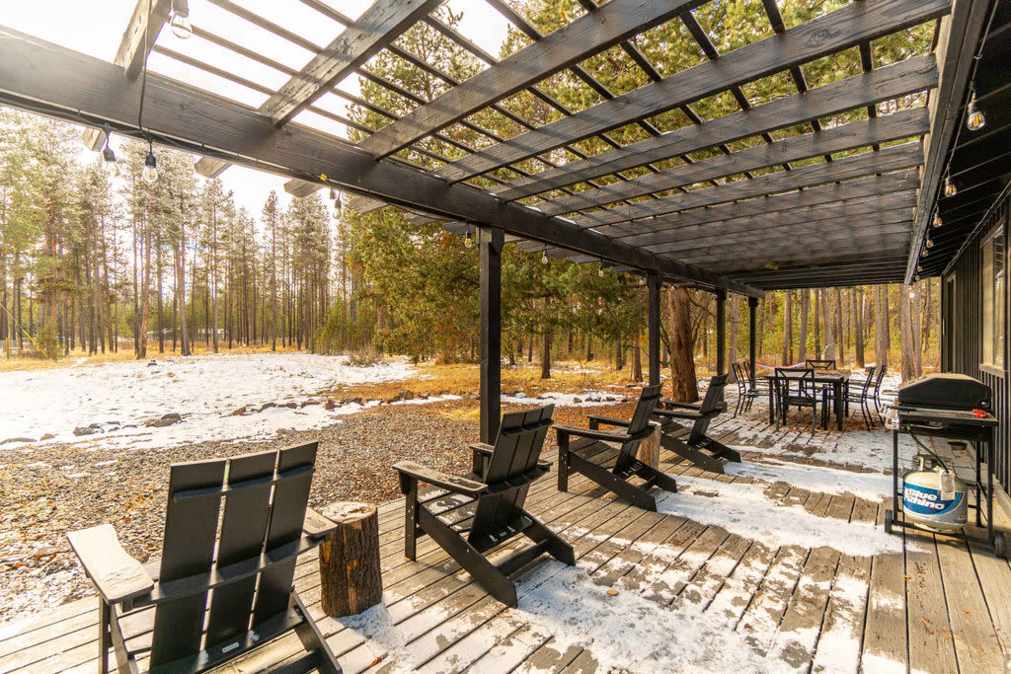 The scene features a black wooden deck with several Adirondack chairs overlooking a snowy landscape filled with trees.