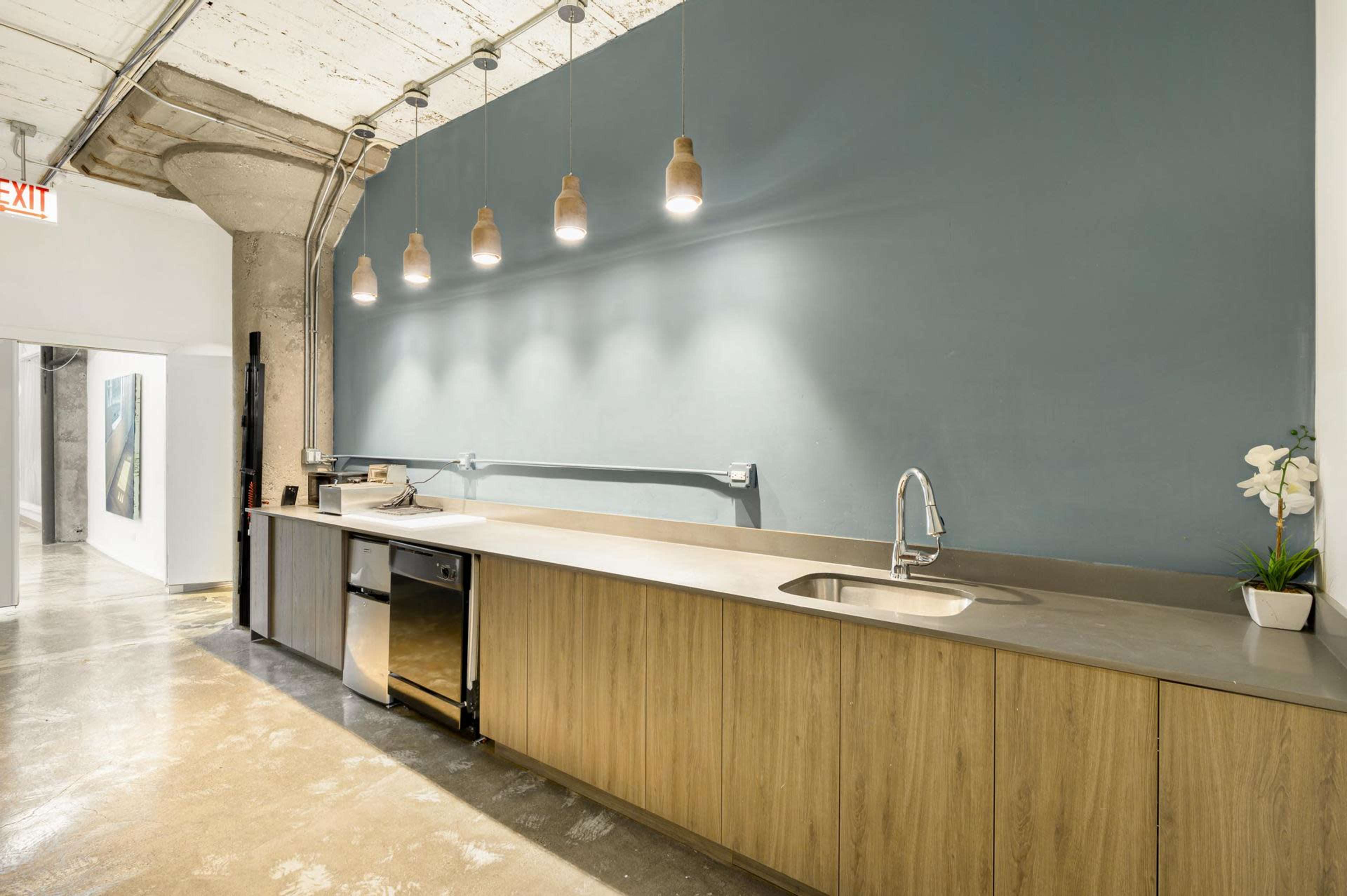 The image shows a modern kitchen with wooden cabinets, a stainless steel sink, and pendant lighting against a blue wall.