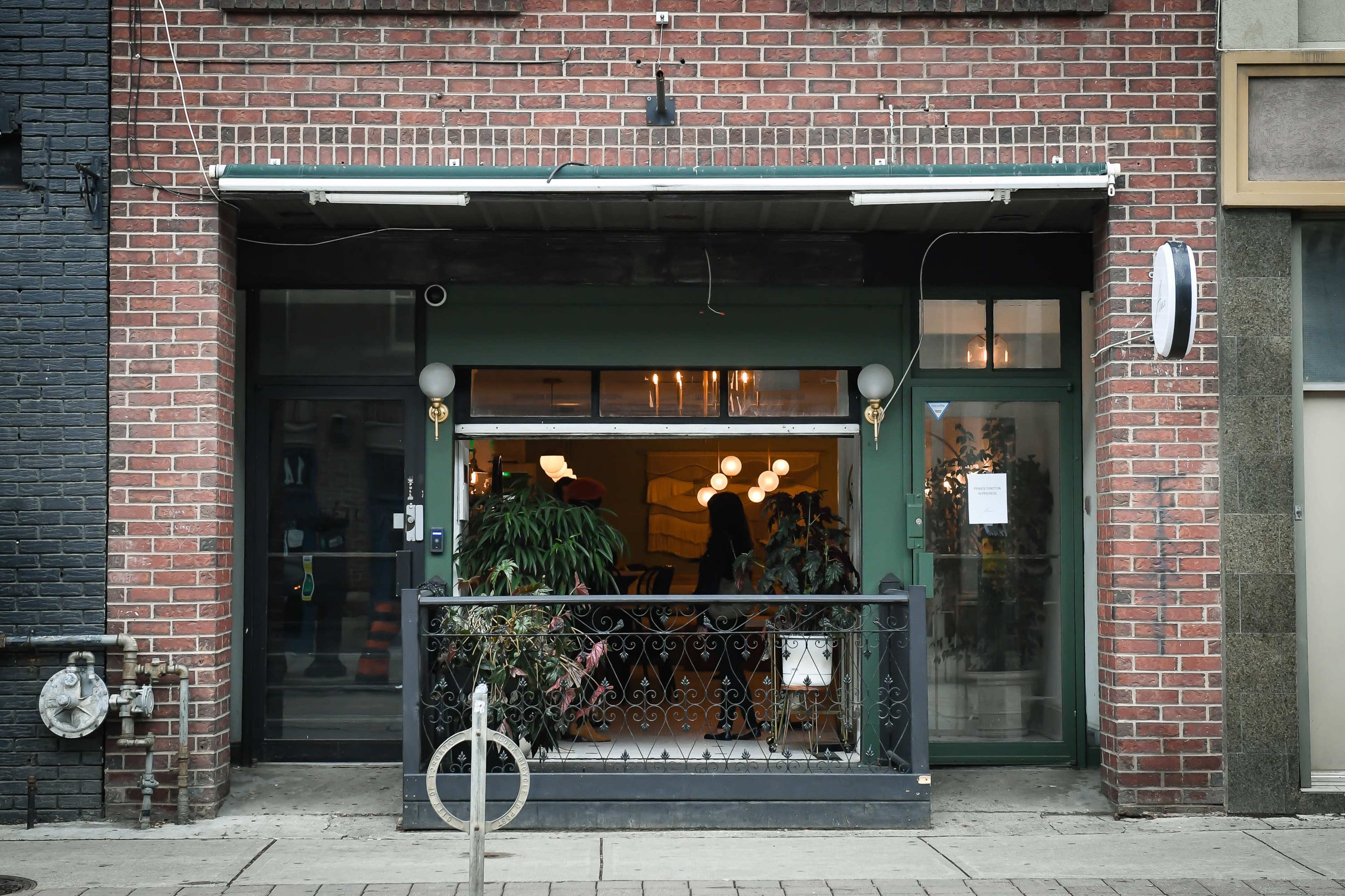 A brick storefront with large glass windows, a small balcony and modern lighting fixtures.